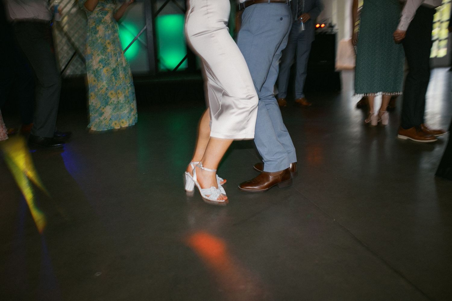 Dance floor at a wedding reception with party lights and silhouetted feet of guests.