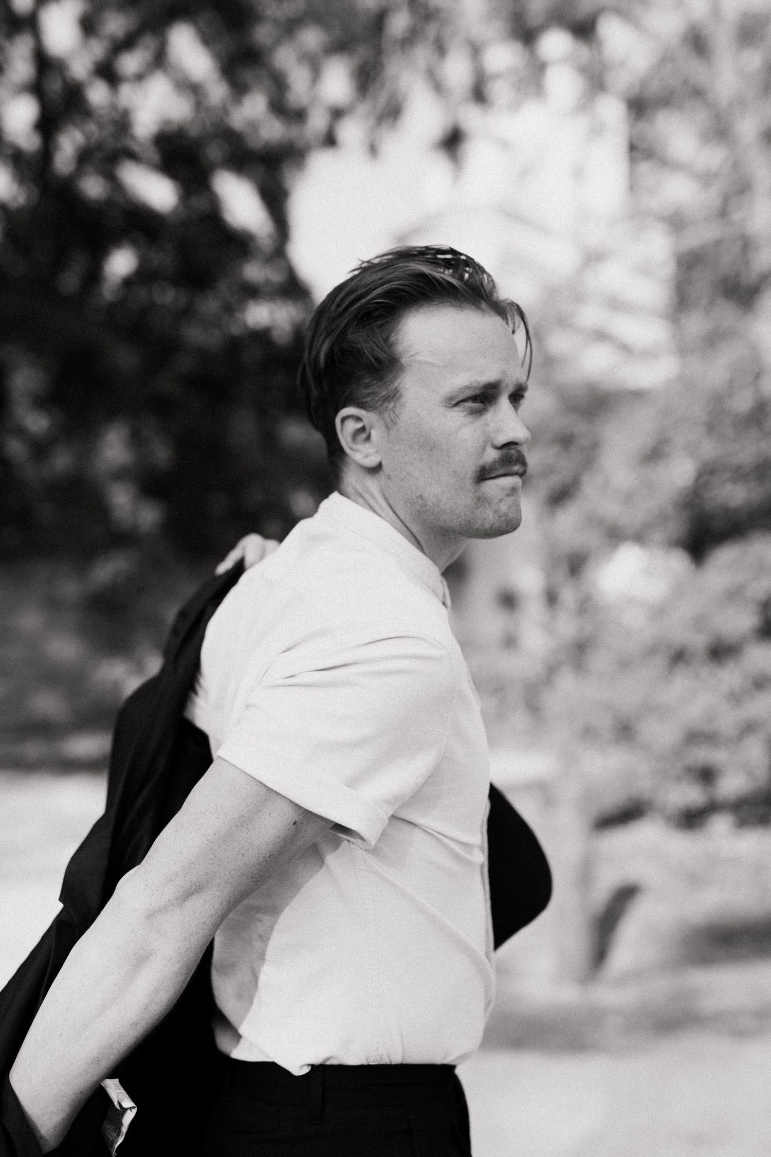 A contemplative portrait of a person in a white shirt with a dark jacket draped over one shoulder.