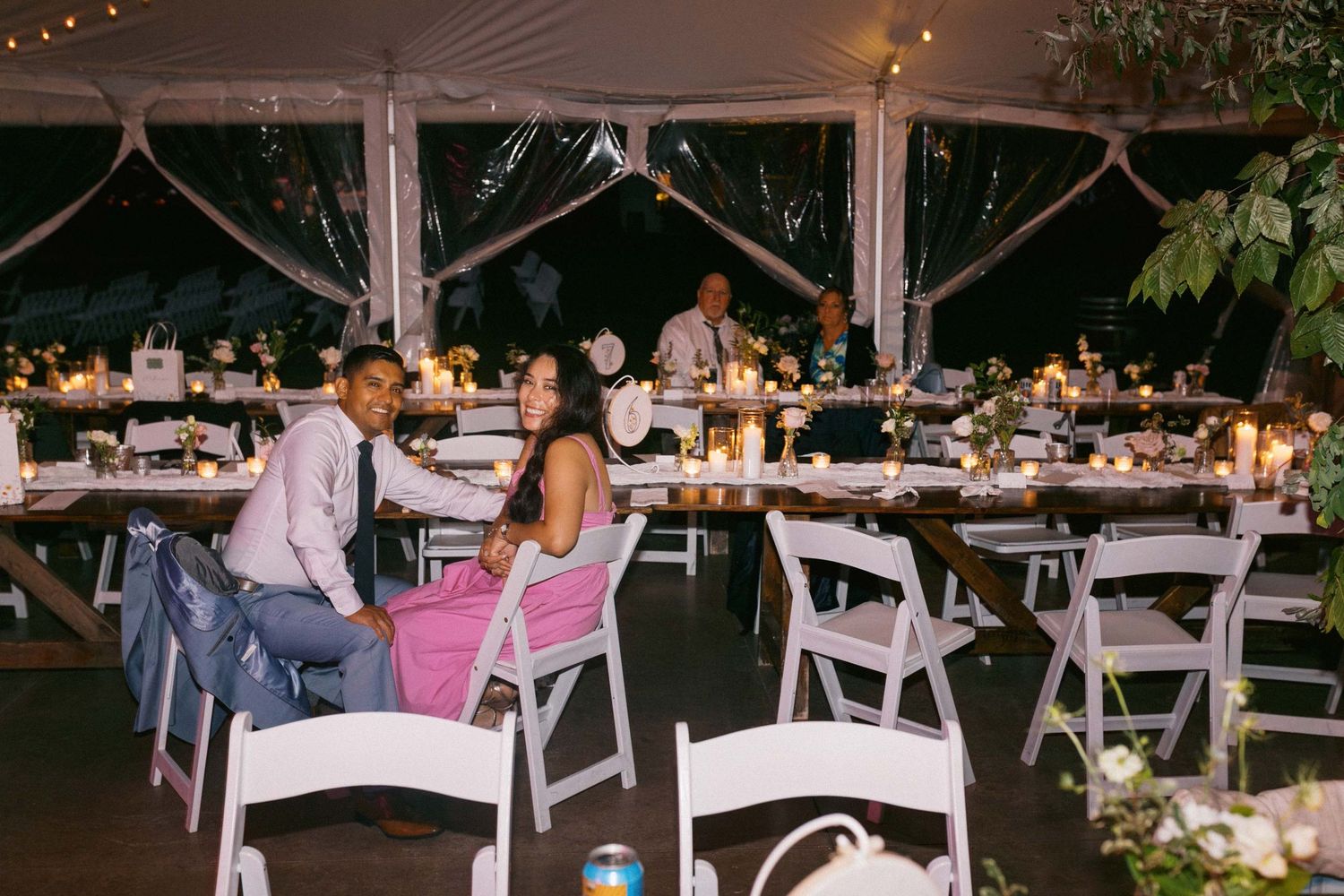 Wedding guests at an outdoor evening wedding reception with white chairs and tables under string lights creating a romantic ambiance.