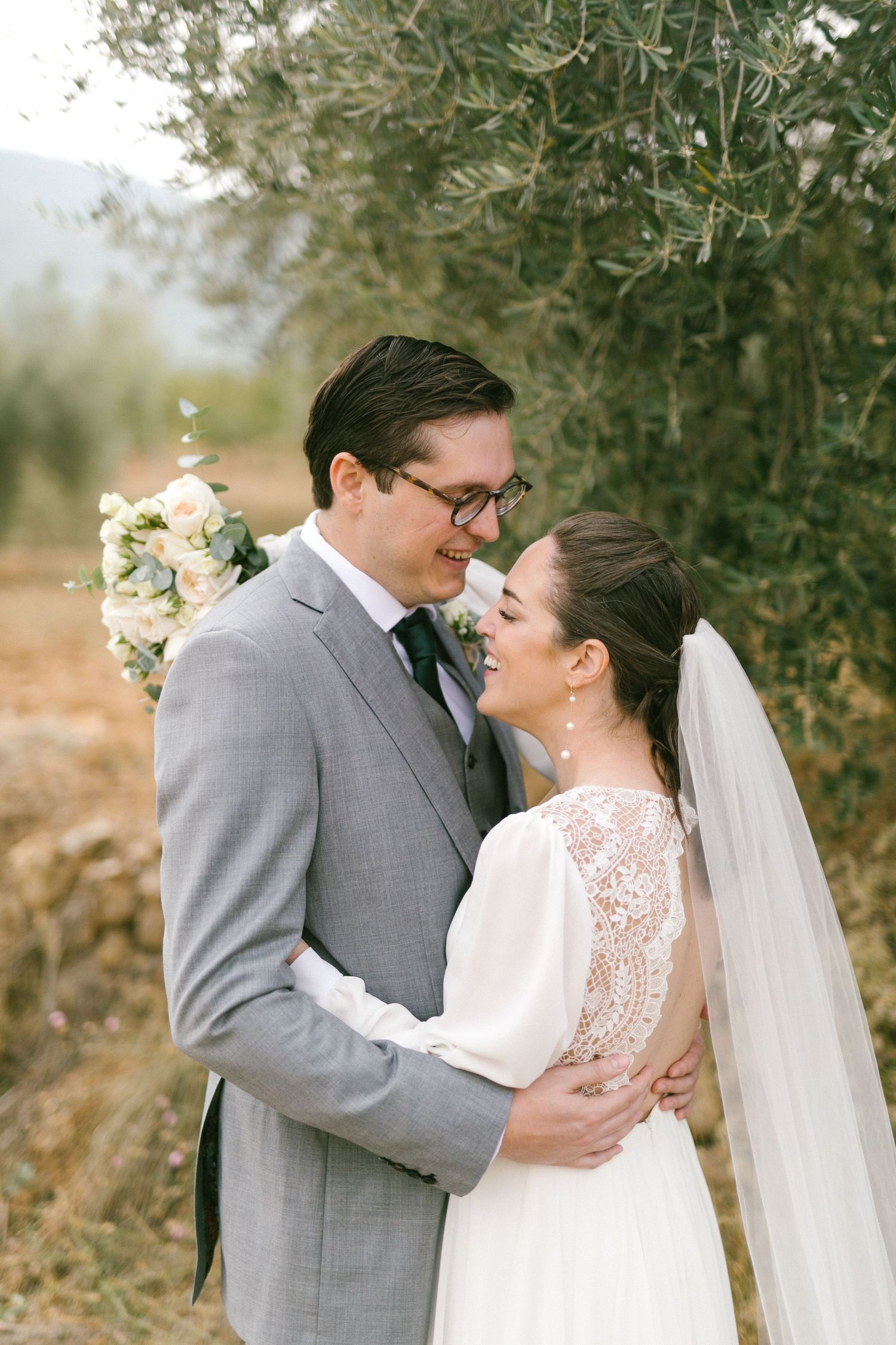 Newly wedded couple sharing an intimate moment outdoors under olive trees on their wedding day.