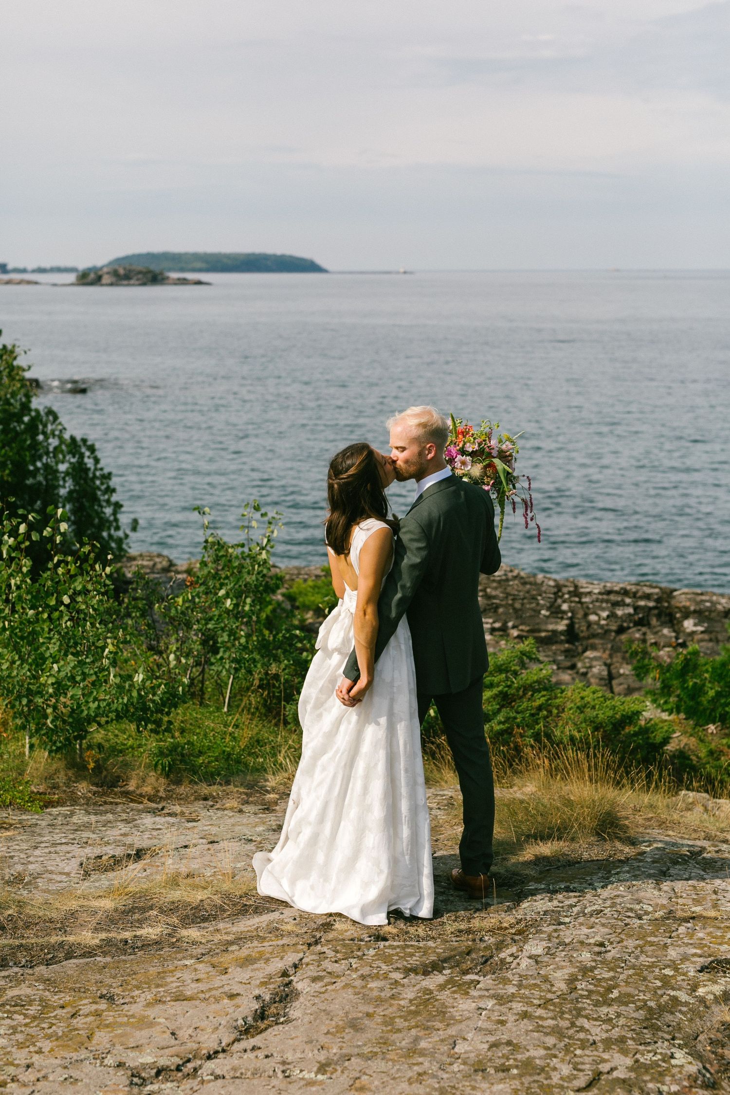 A couple shares an intimate moment on rocky coastal cliffs overlooking a scenic ocean view.