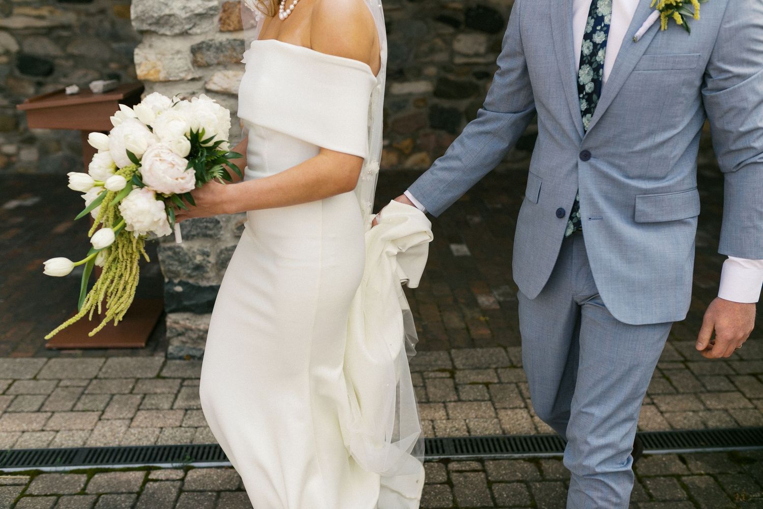 A close-up of a bride in white dress holding bouquet next to person in light blue suit.