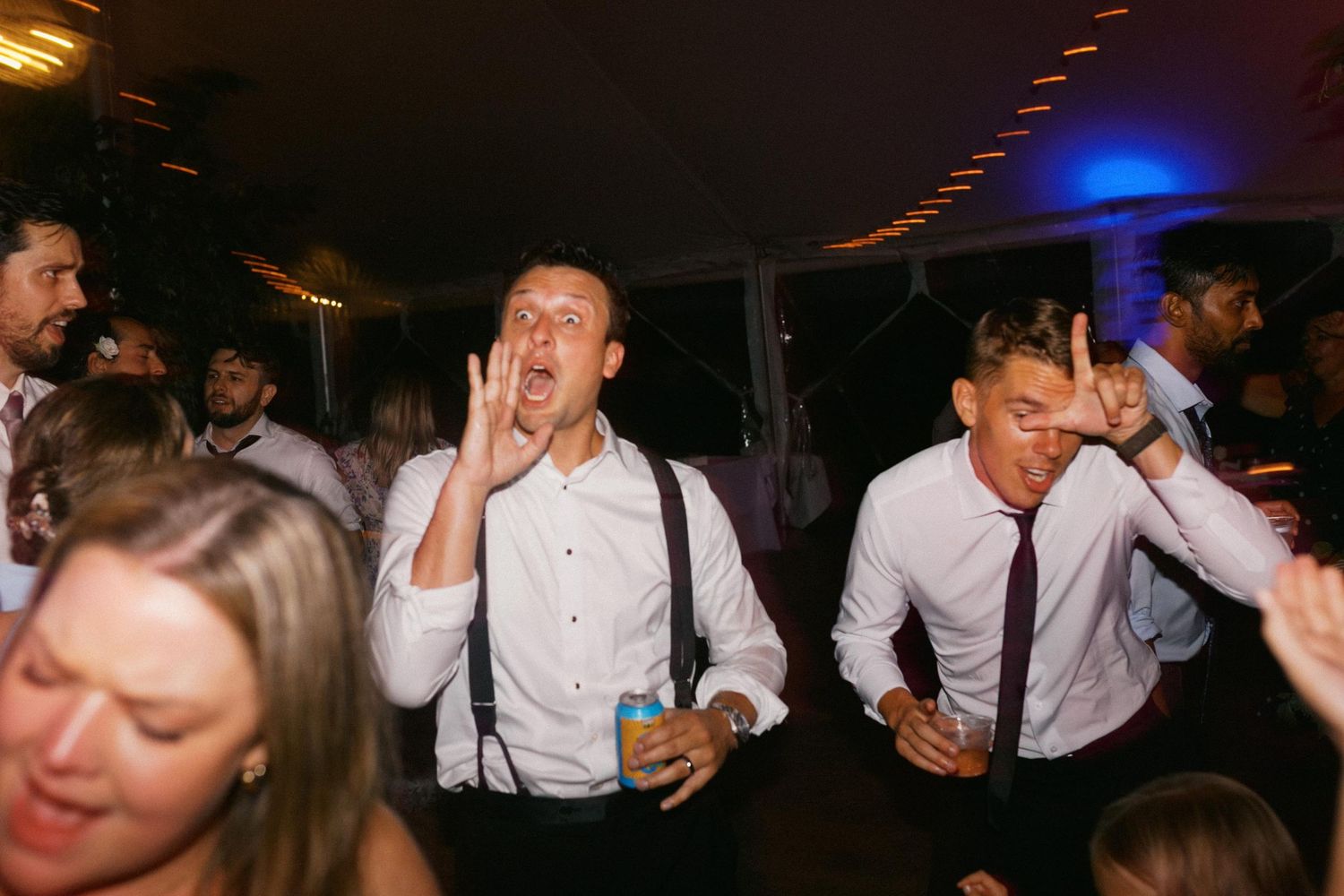 Wedding guests dance and celebrate together on a dimly lit dance floor during an energetic reception party.