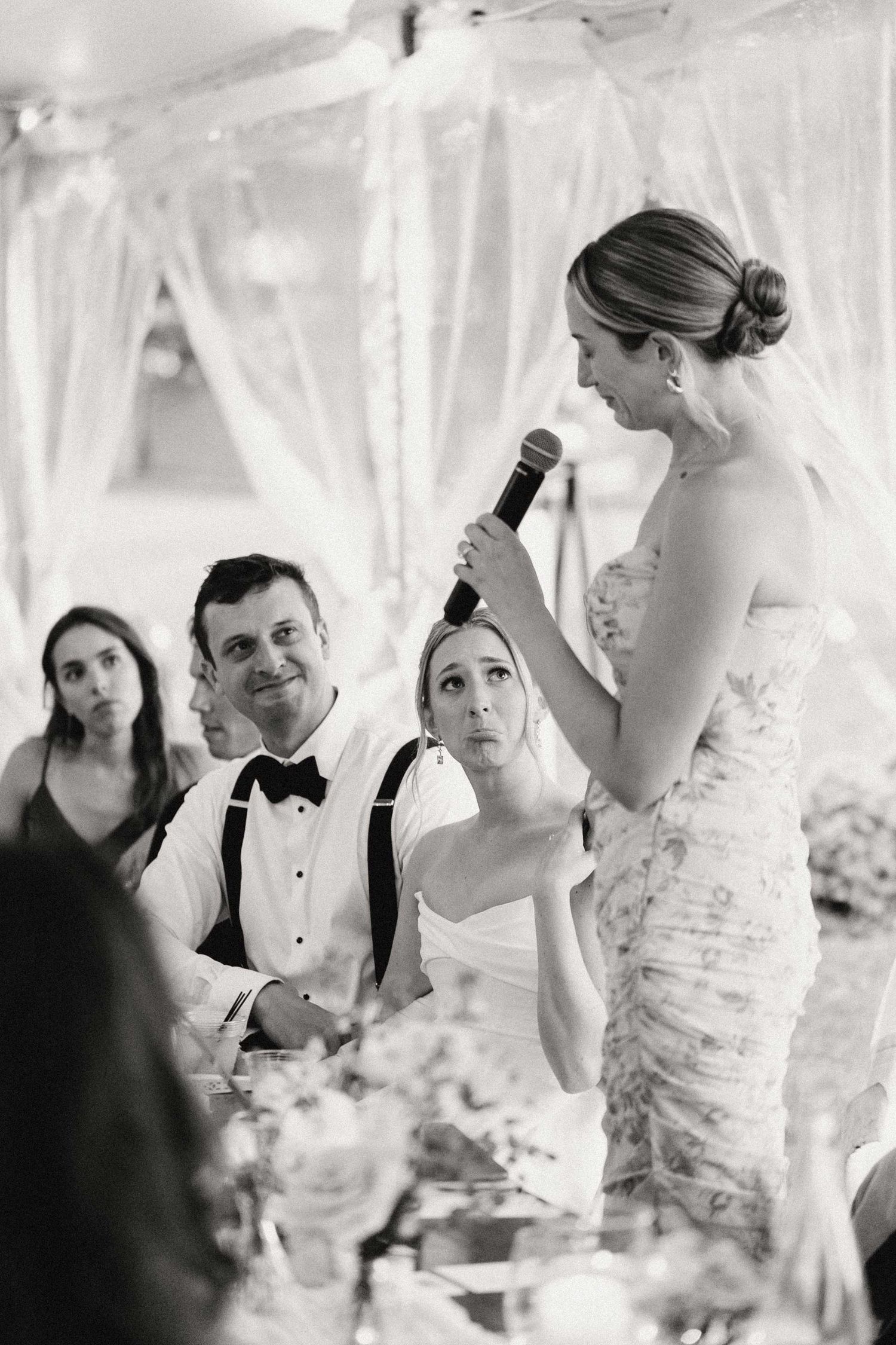 Black and white wedding reception photo series showing candid moments between guests and the couple in a tented venue.