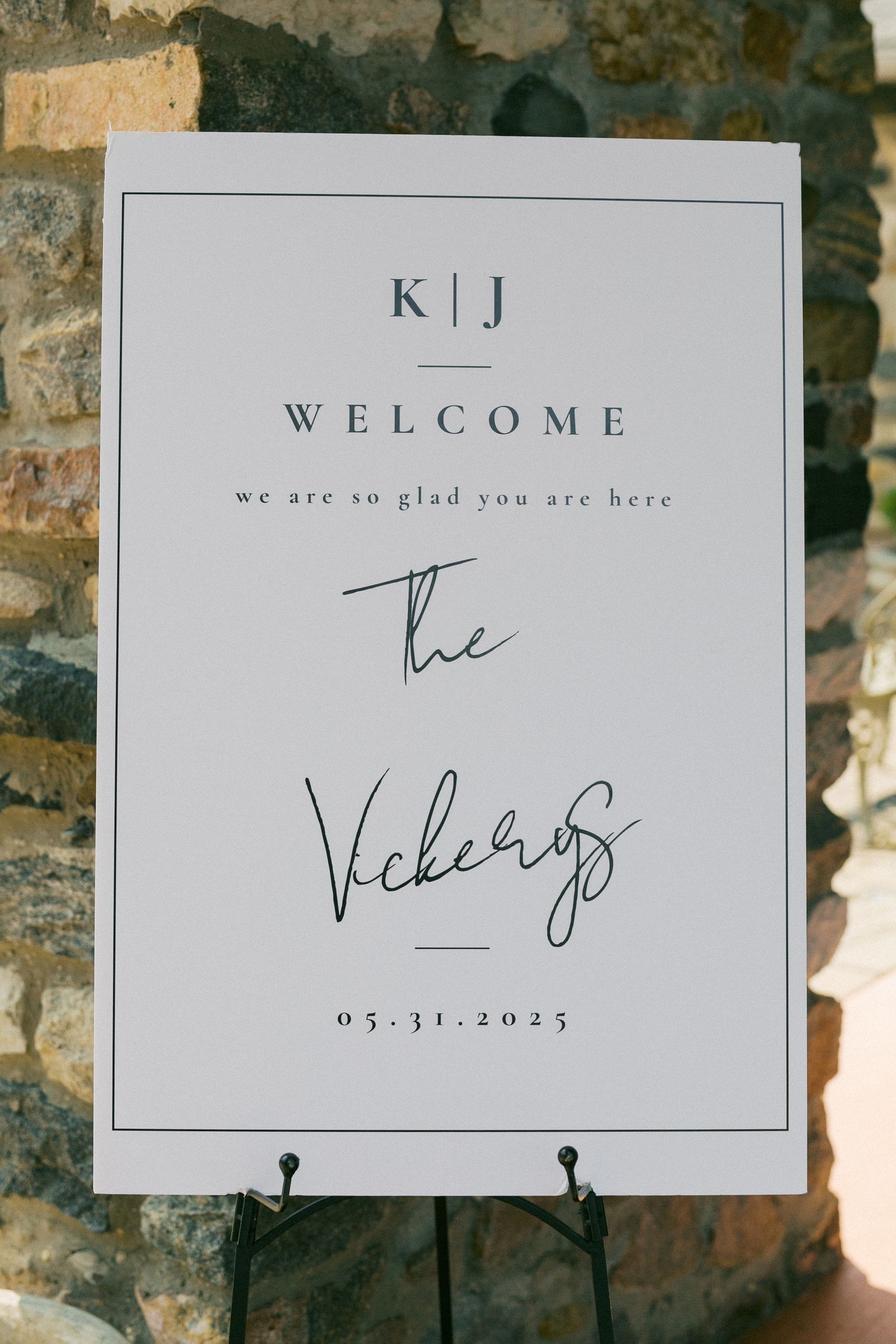 Simple white wedding welcome signs with elegant text and calligraphy on a stone wall background.