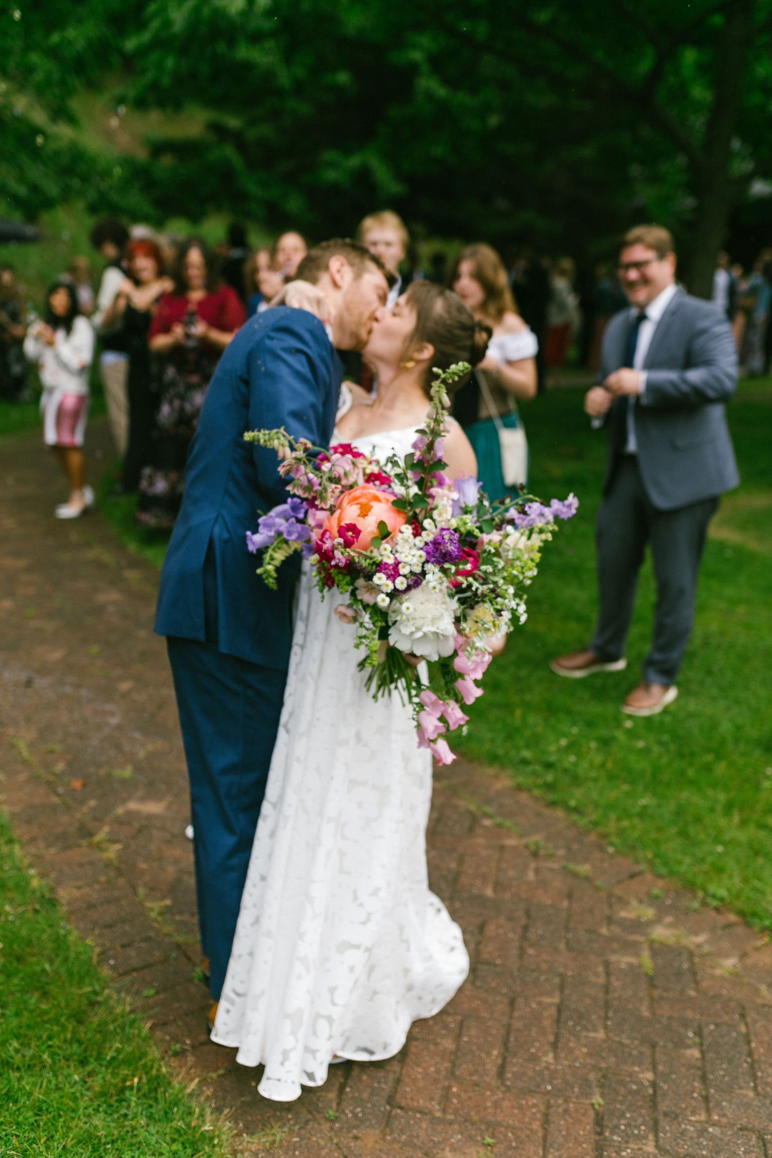 A couple shares a romantic kiss on their wedding day while holding a vibrant wildflower bouquet.