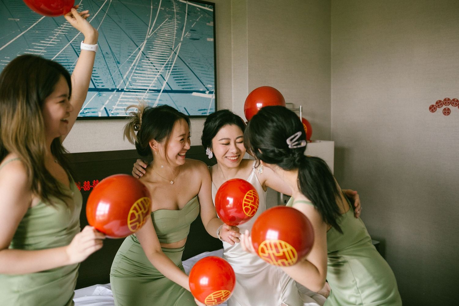 Bridesmaids in sage green dresses celebrate with red balloons featuring gold Chinese characters at a wedding.