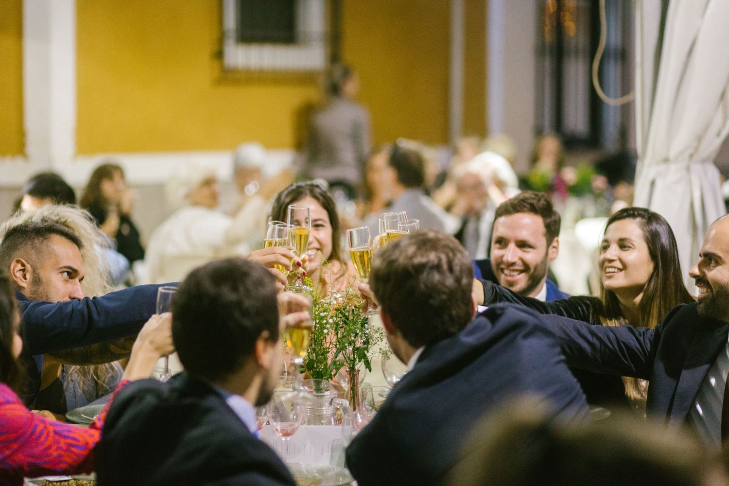 Celebratory dinner party guests raising glasses for a toast at an outdoor reception.