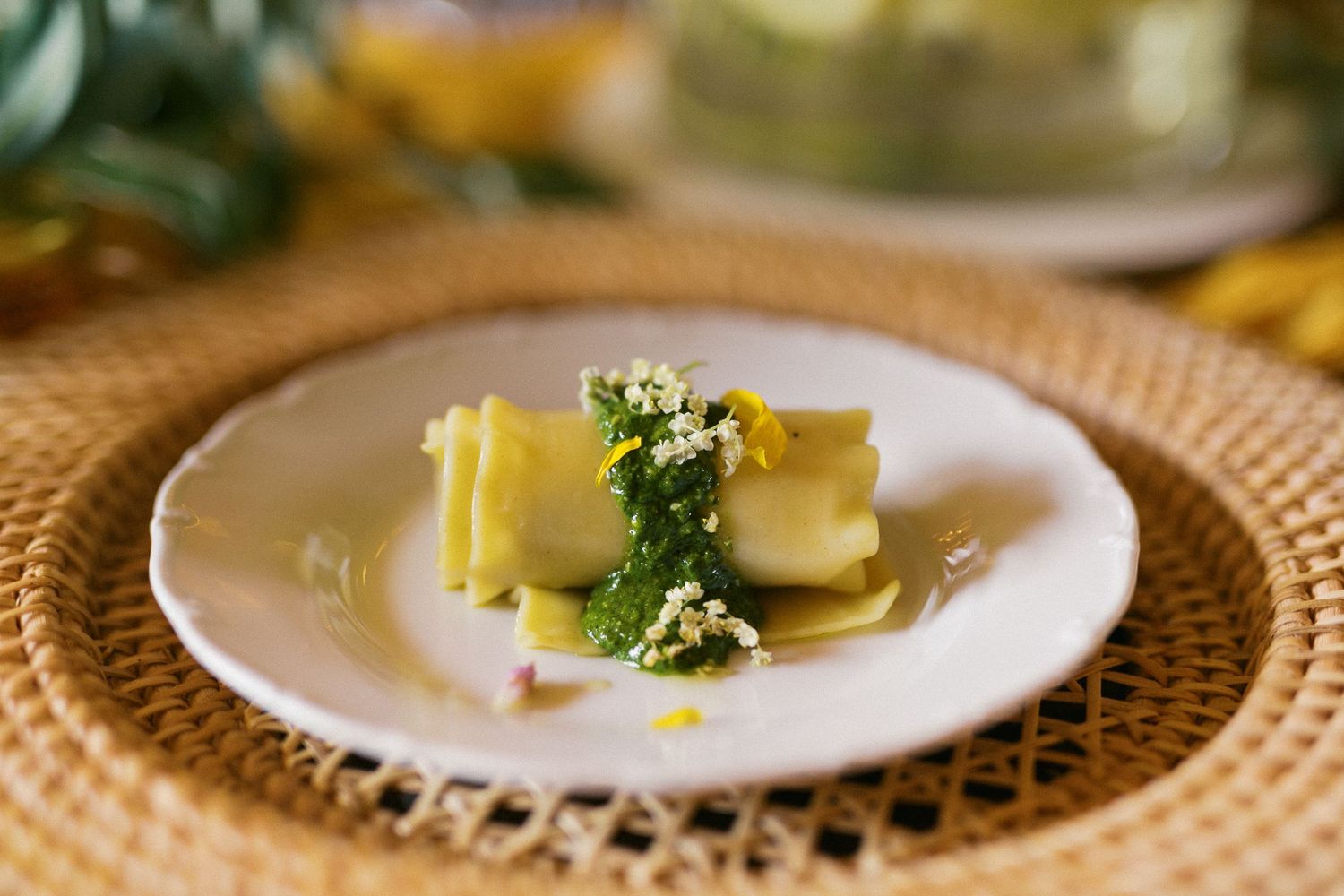 Elegant lasagna pasta dish garnished with fresh herbs and edible flowers on a white plate atop a woven placemat.