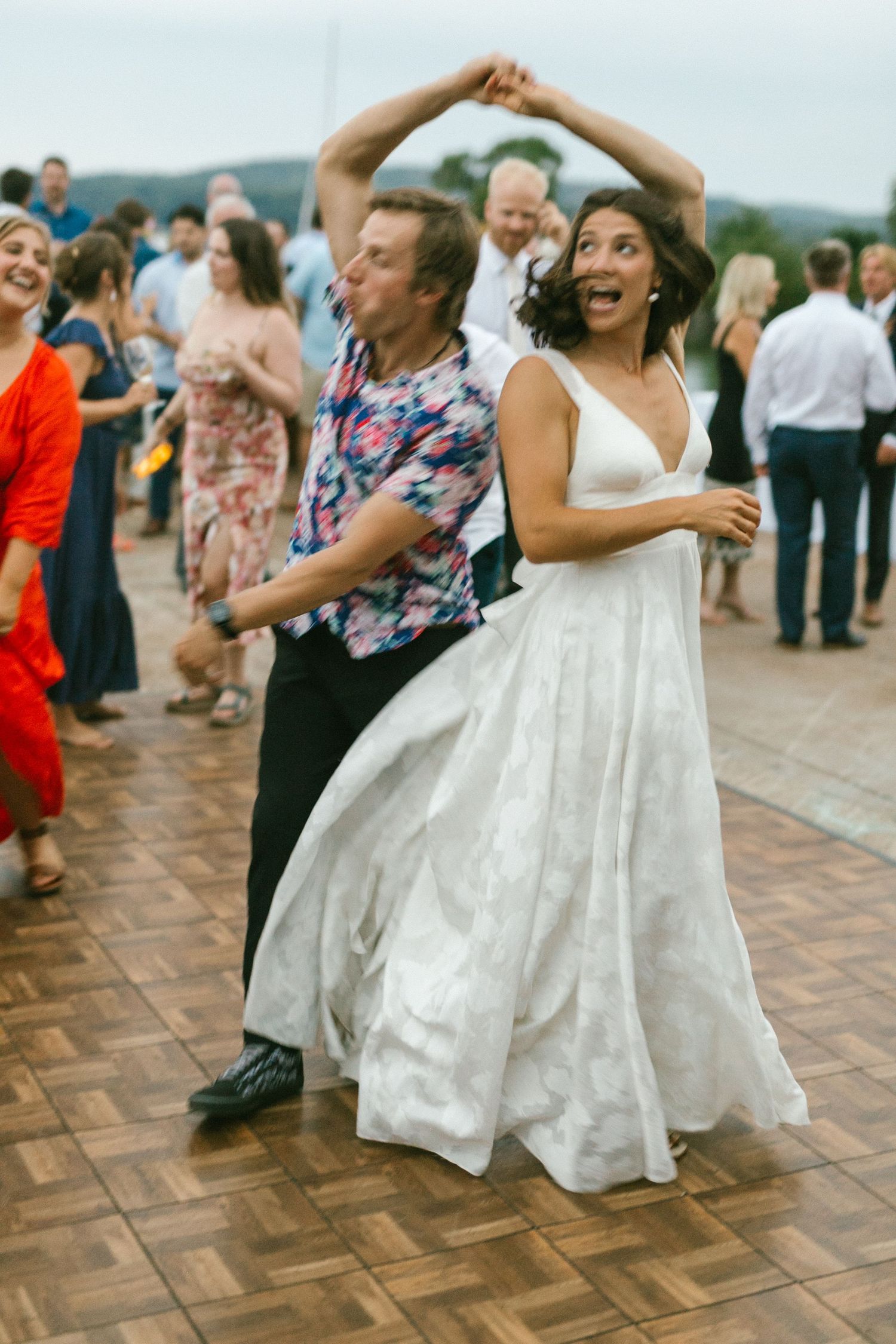Wedding guests dance joyfully on a wooden dance floor during a lively reception celebration.