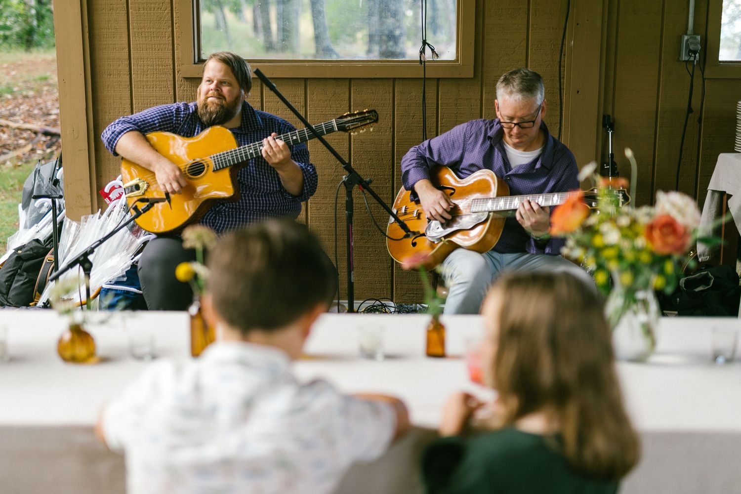 Two musicians performing with acoustic guitars at an outdoor wedding reception.