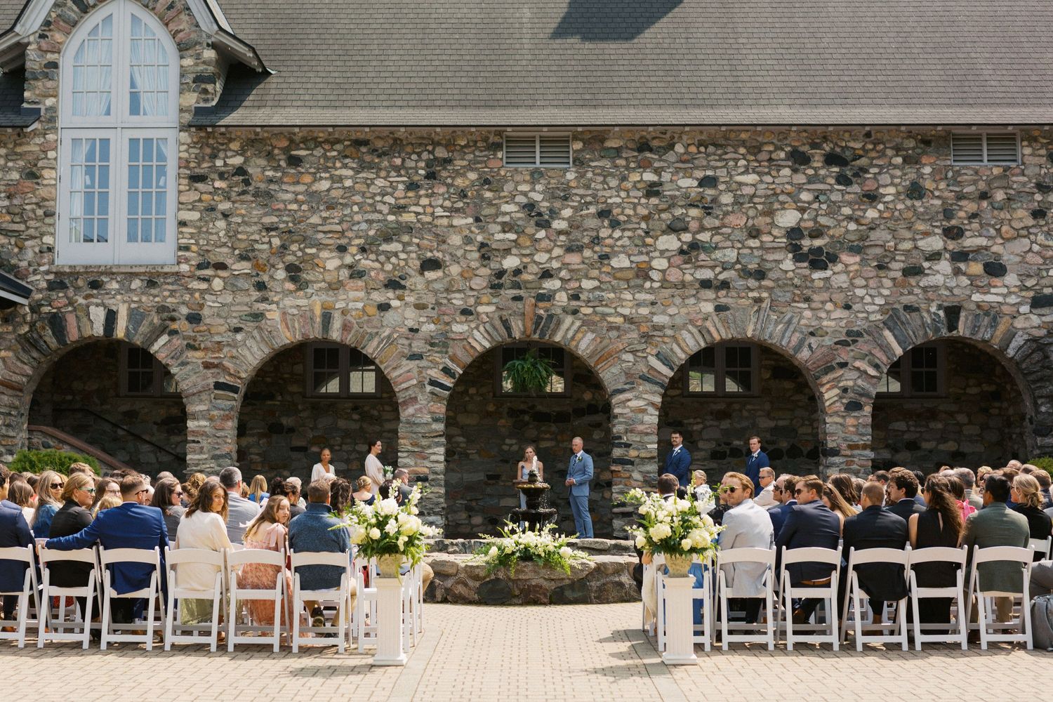 Stone chapel exterior with white chairs set up for an outdoor wedding ceremony.