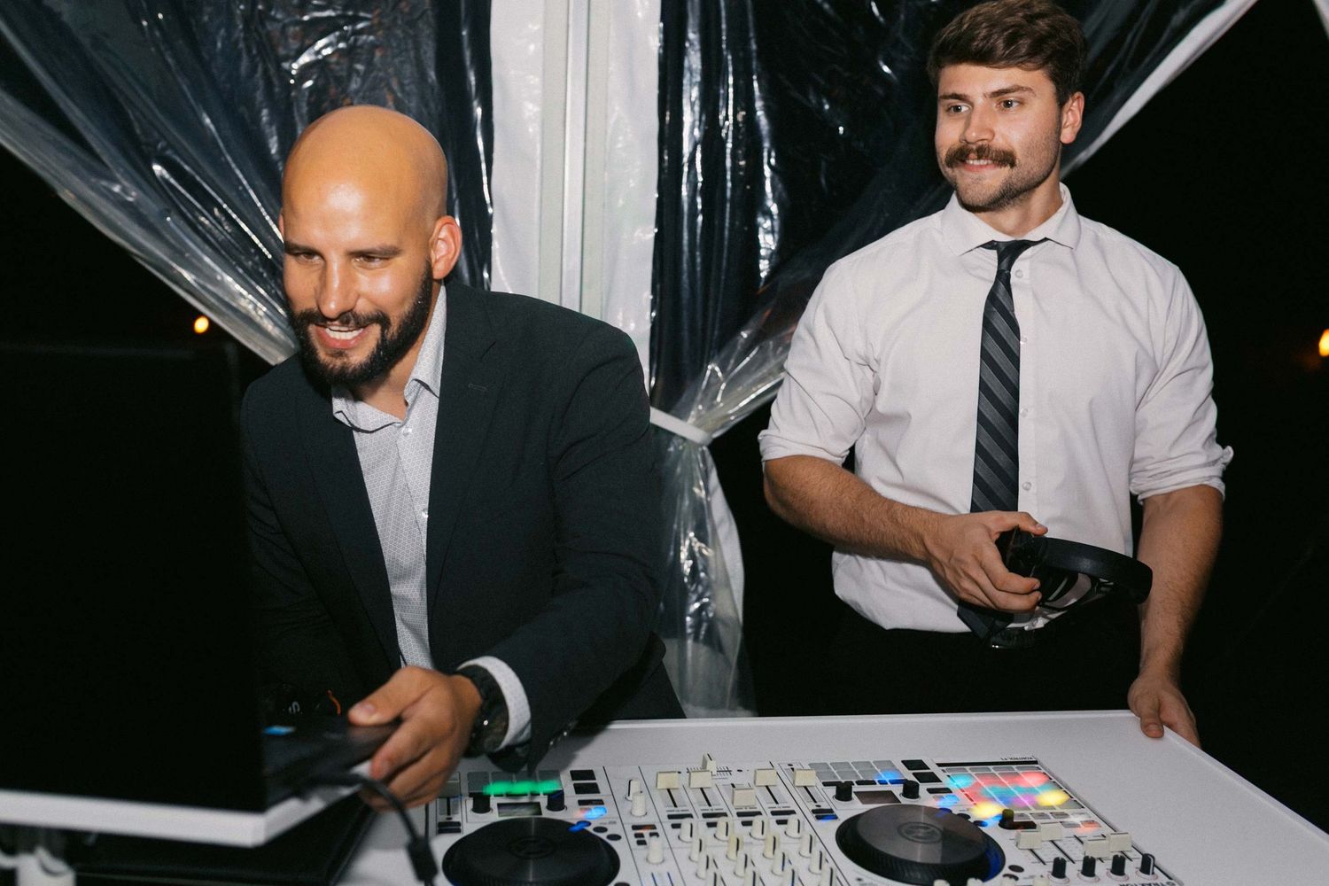 DJ performs on stage with mixing equipment and turntables at a nightclub event.