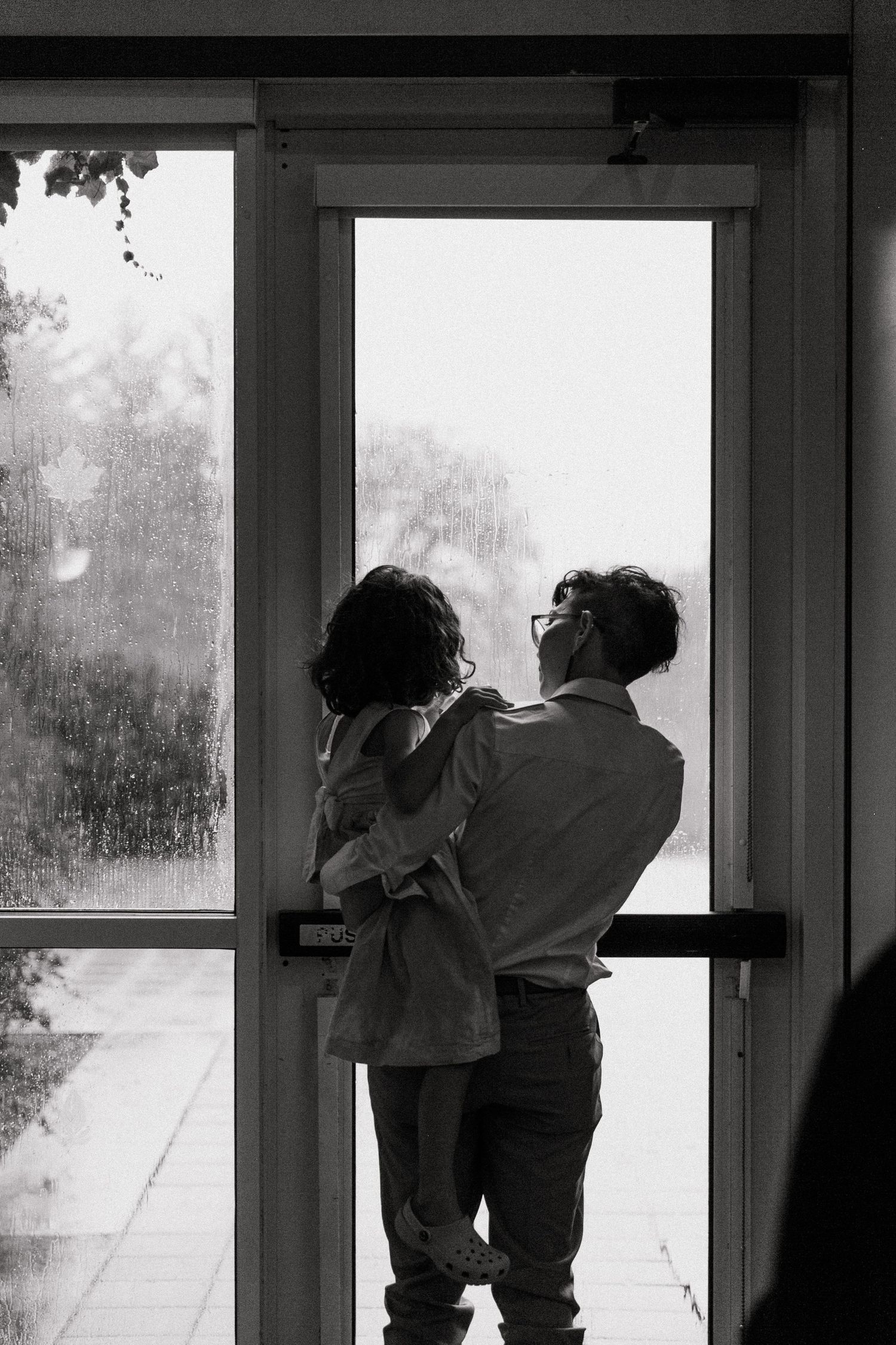 Black and white silhouette of man holding child near glass door in emotional tender moment.
