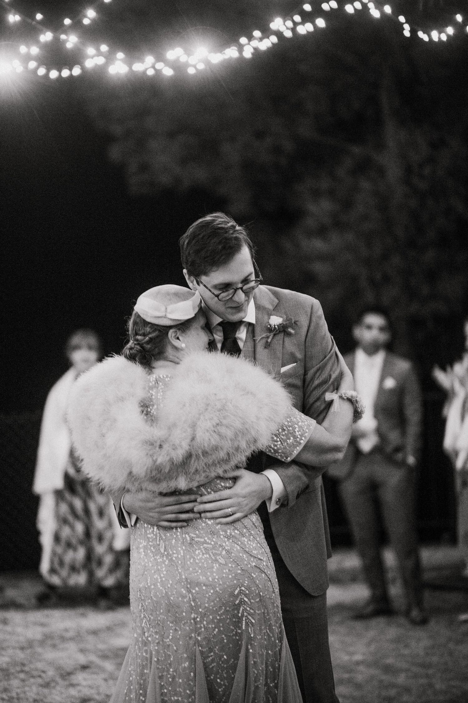 A couple shares an intimate dance moment under twinkling lights at an outdoor evening celebration.