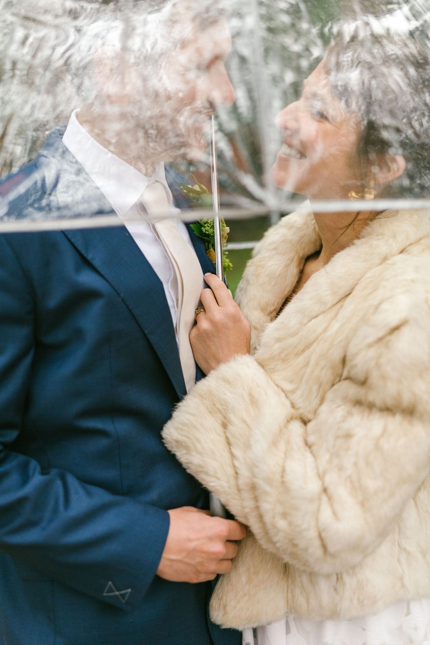 A couple in formal attire sharing an intimate moment while vaping or smoking, with one wearing a blue suit and cream fur coat.