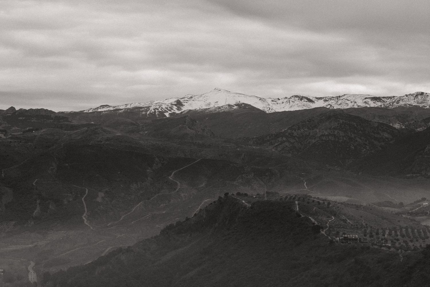 Dramatic black and white mountain landscape with snow-capped peaks and misty valleys under cloudy skies.