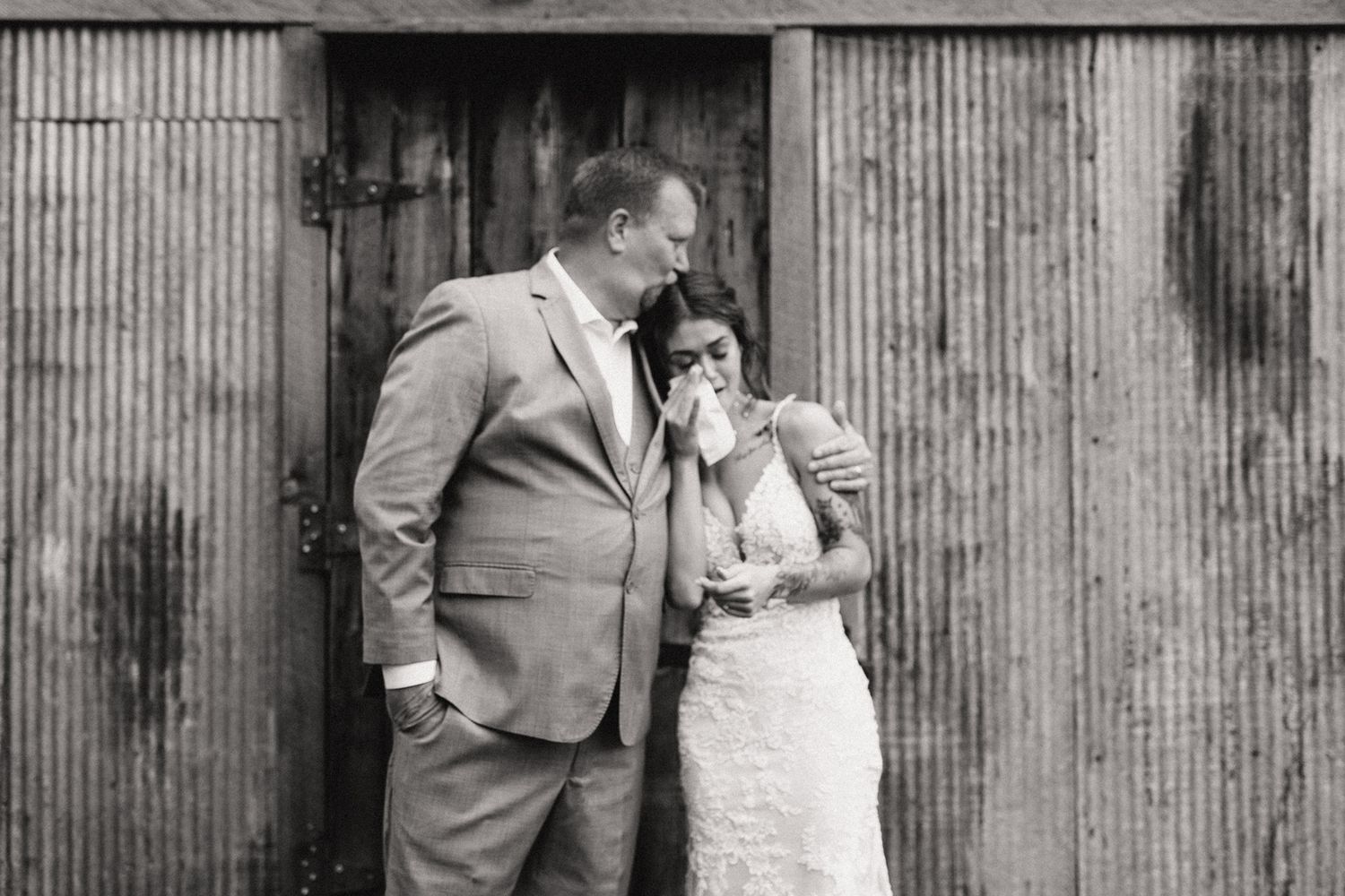Black and white photo of groom comforting emotional bride outside rustic barn.