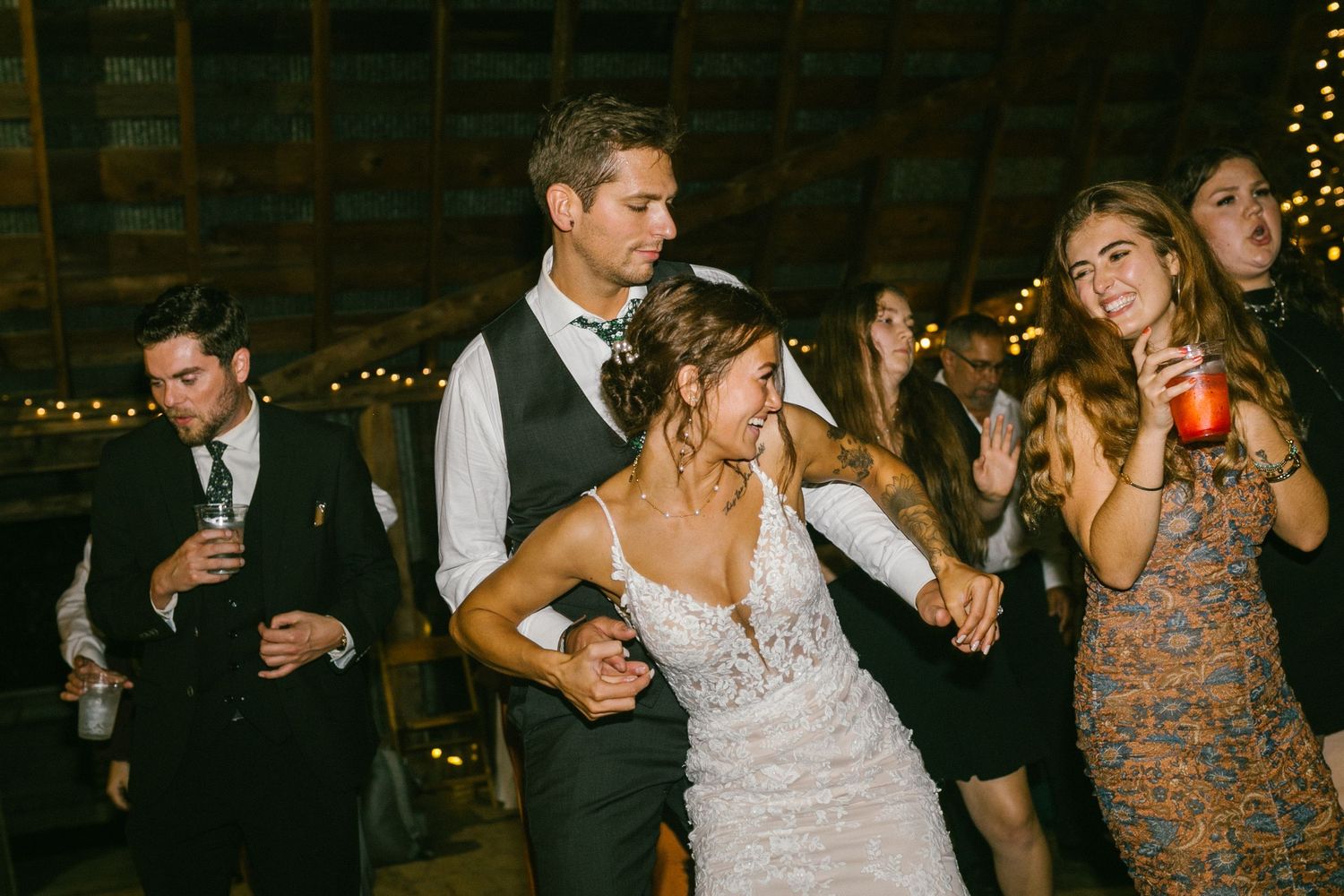 Bride and groom dancing at night with holiday string lights glowing in the rustic barn venue background.