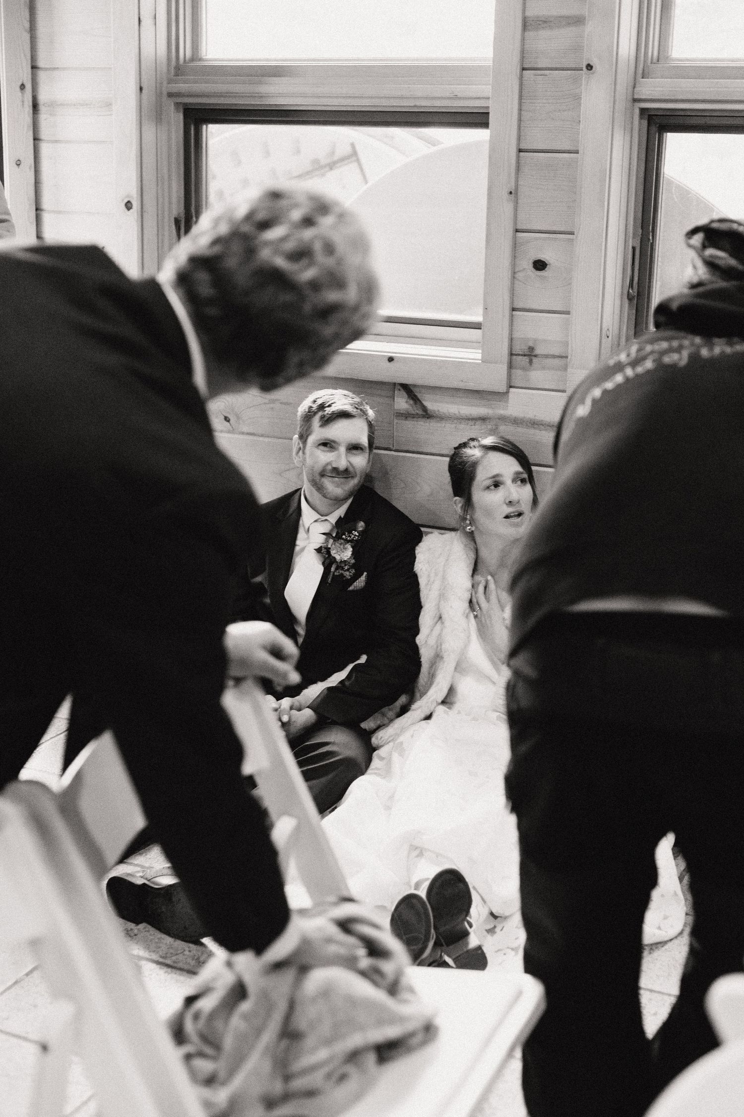A black and white photo of a happy couple in wedding attire sitting together during a candid moment.