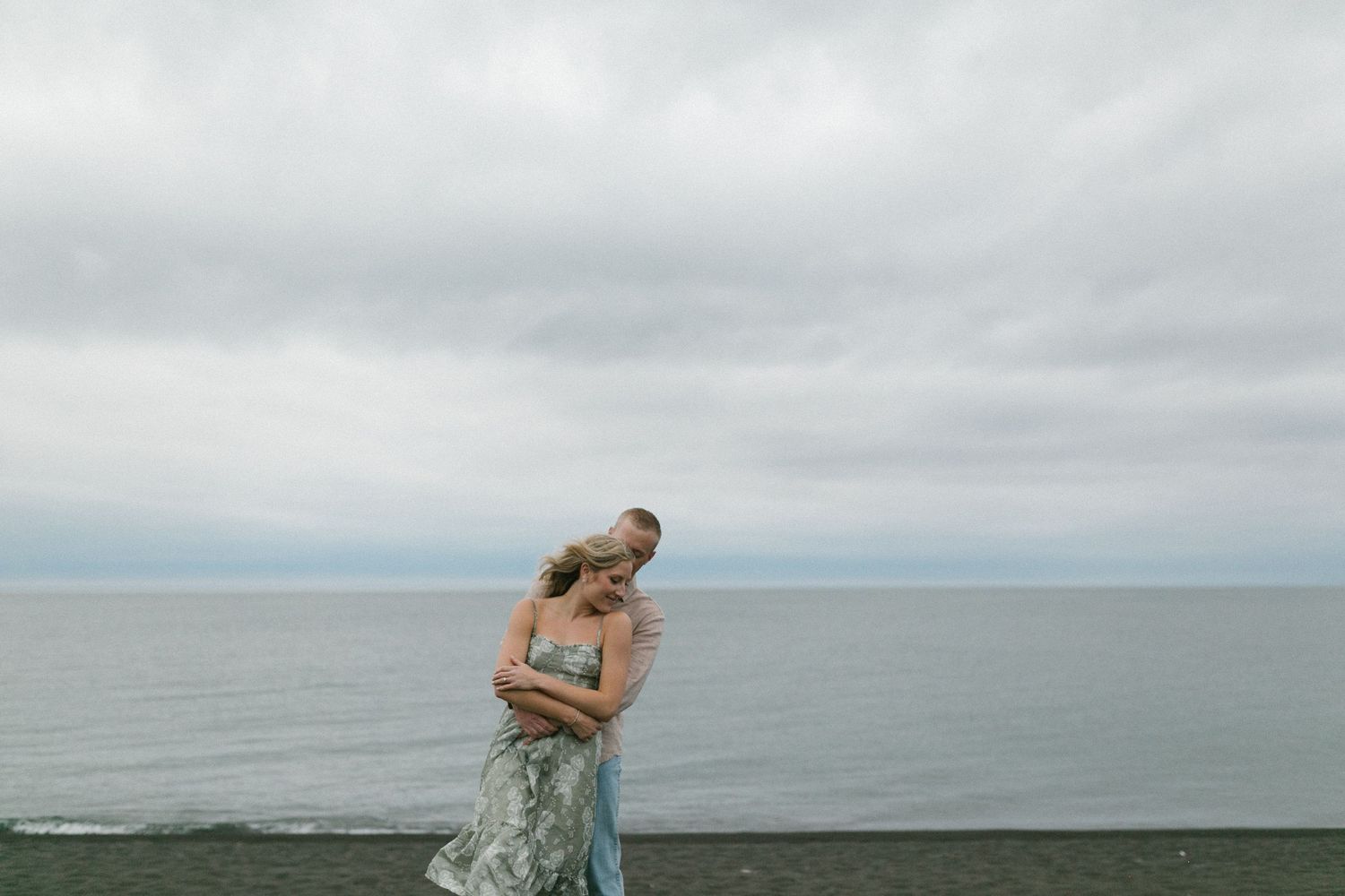 Couple in romantic embrace overlooking ocean on cloudy day.