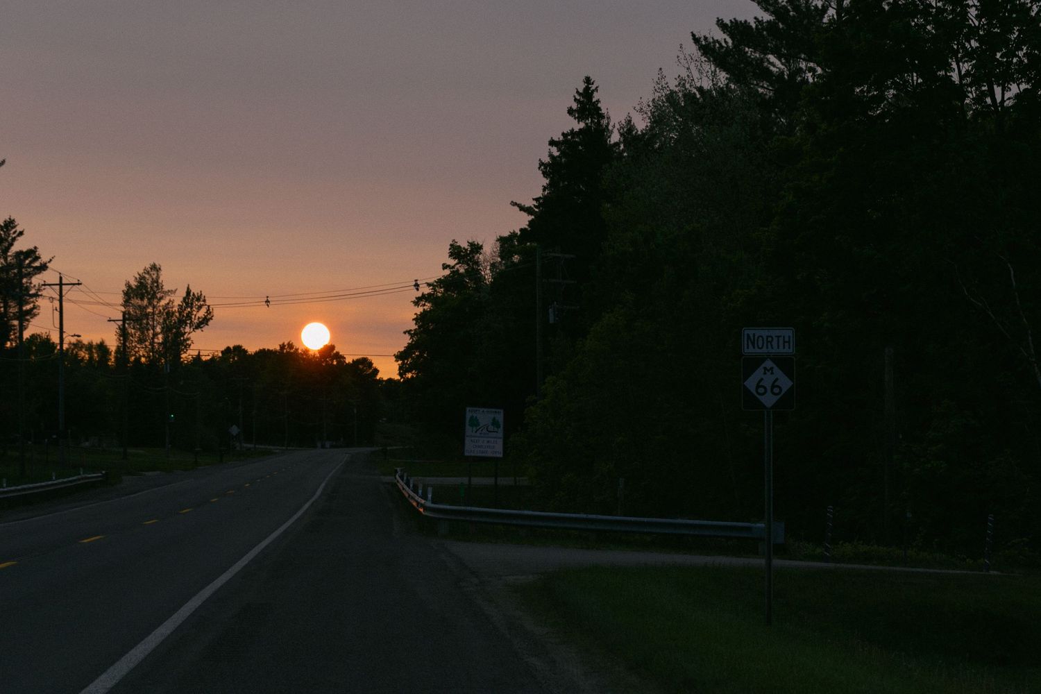 Scenic sunset views along a winding forest road with golden sunlight filtering through the trees.