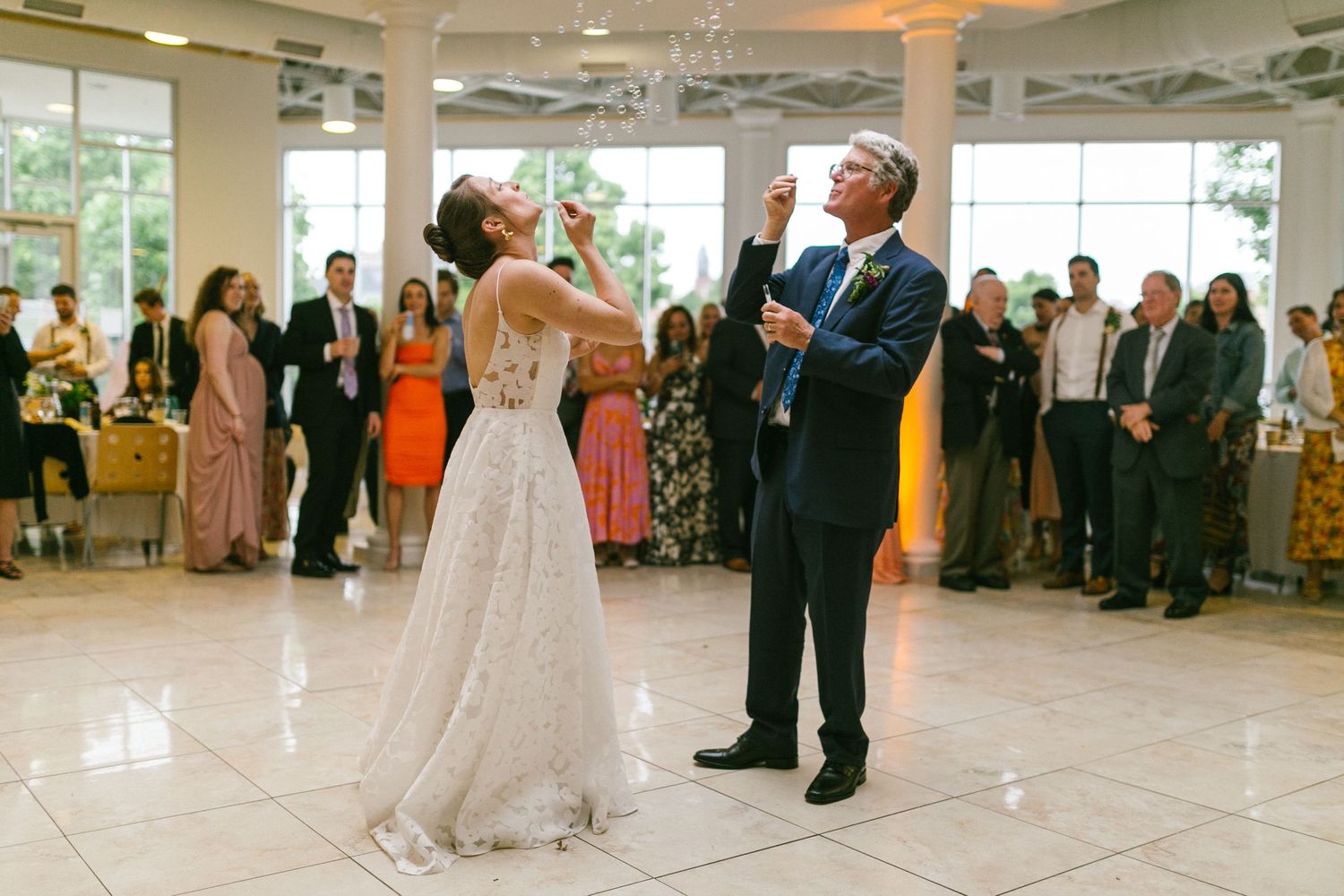 A couple shares their first dance at a wedding reception surrounded by guests in a bright ballroom.