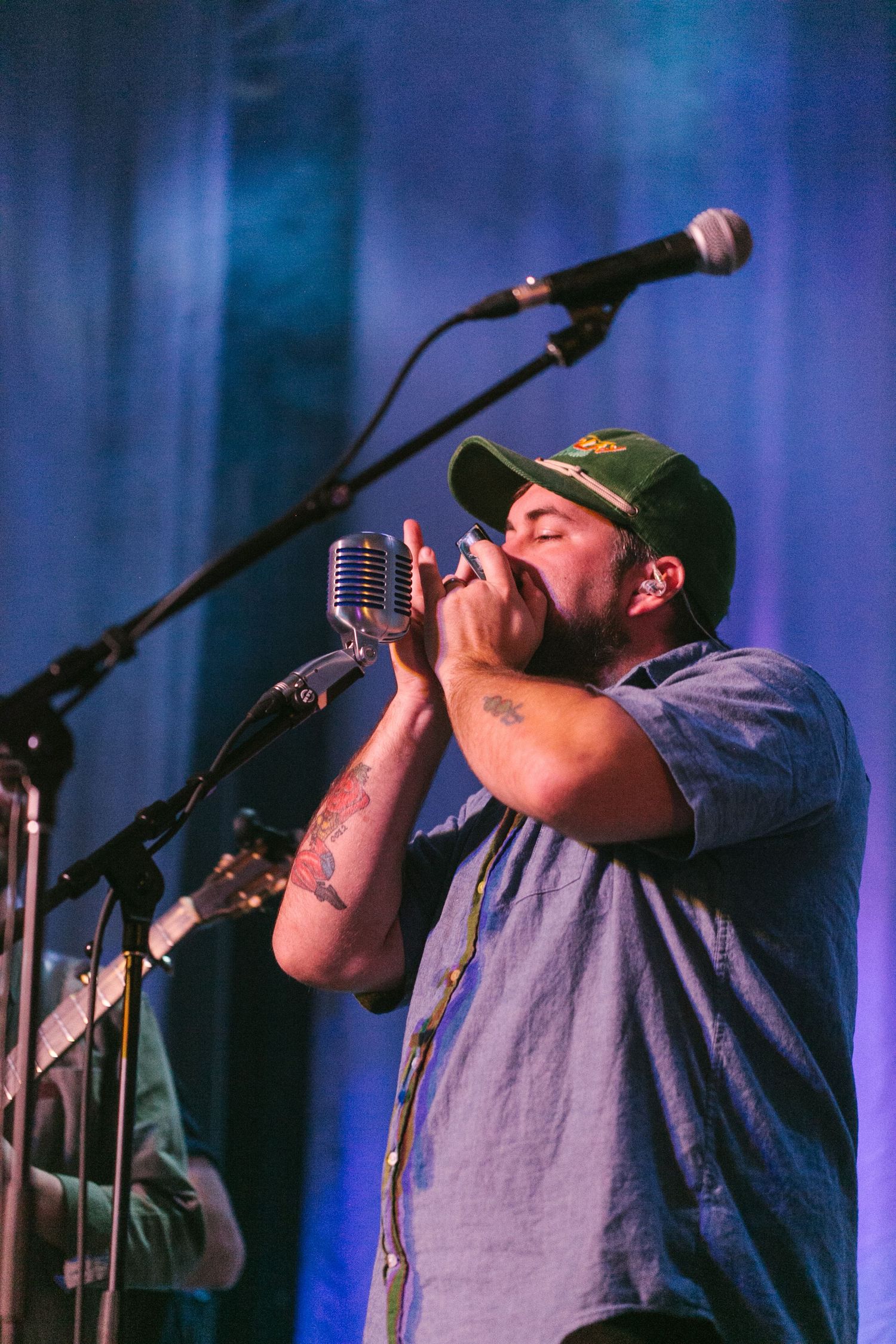 A performer sings passionately into vintage and modern microphones on stage with blue lighting in the background.