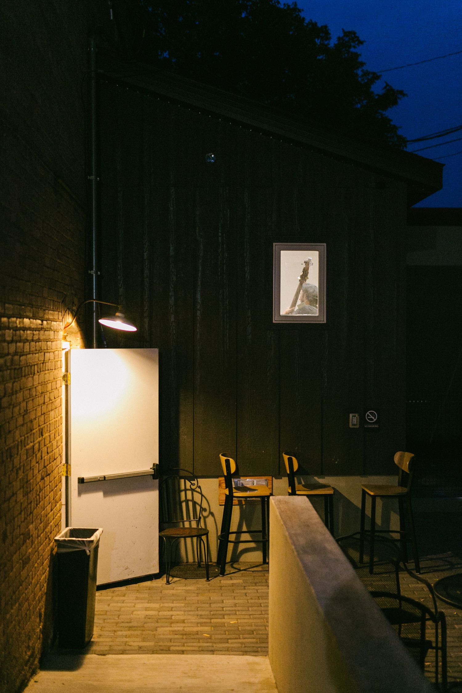 Dimly lit brick wall restaurant interior with wooden chairs and tables under a framed artwork at night.