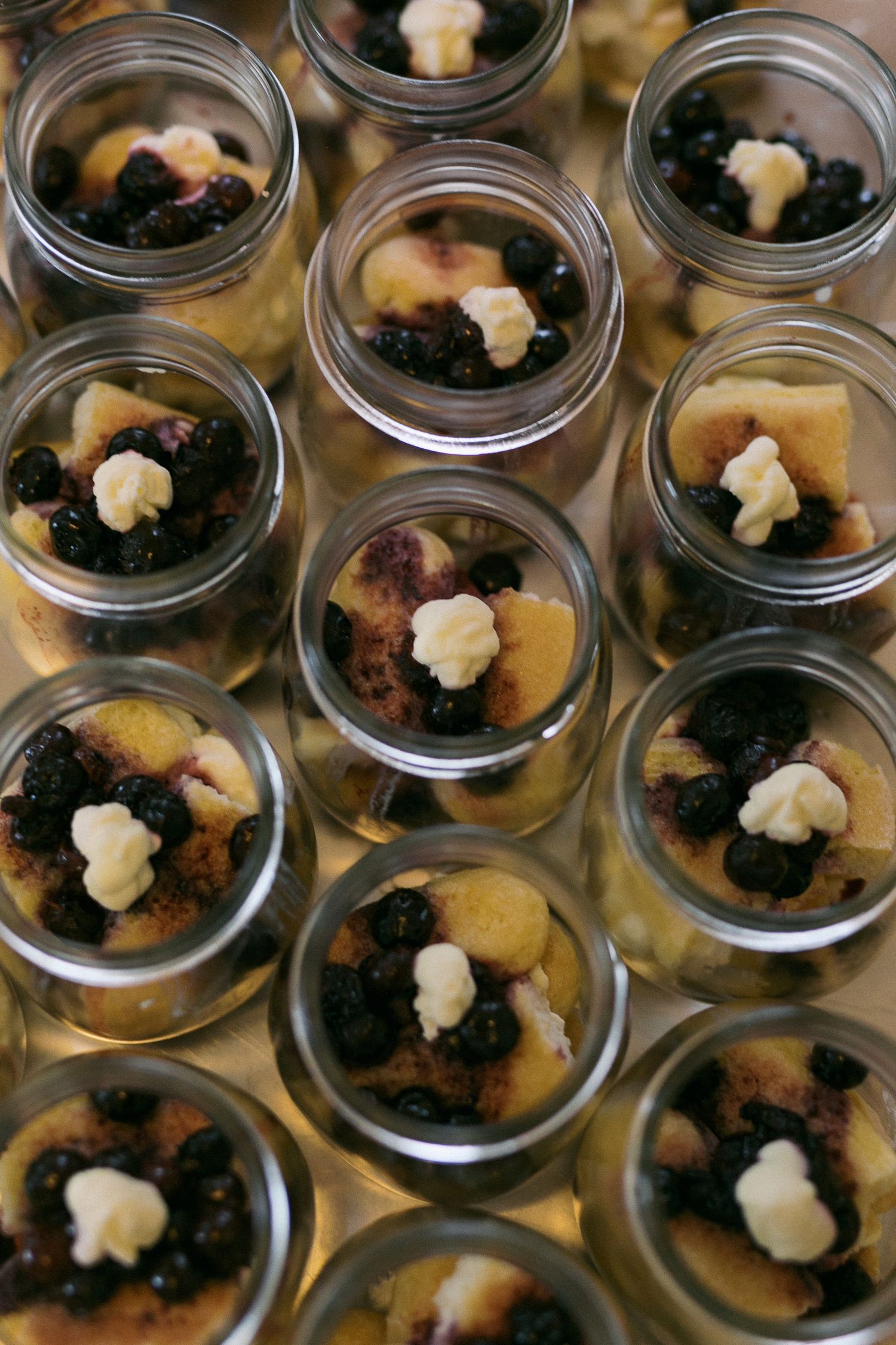 Mason jars filled with blueberry cobbler desserts topped with whipped cream, arranged in rows for a catered event.