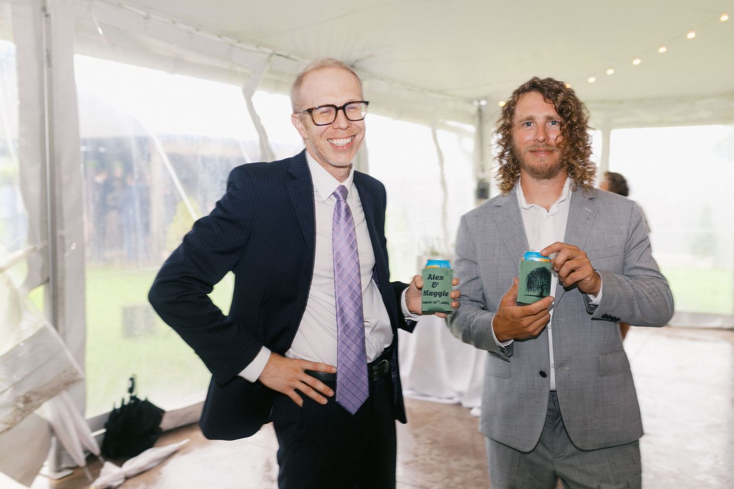 People in formal attire socializing and holding drinks at an indoor event with bright natural lighting.