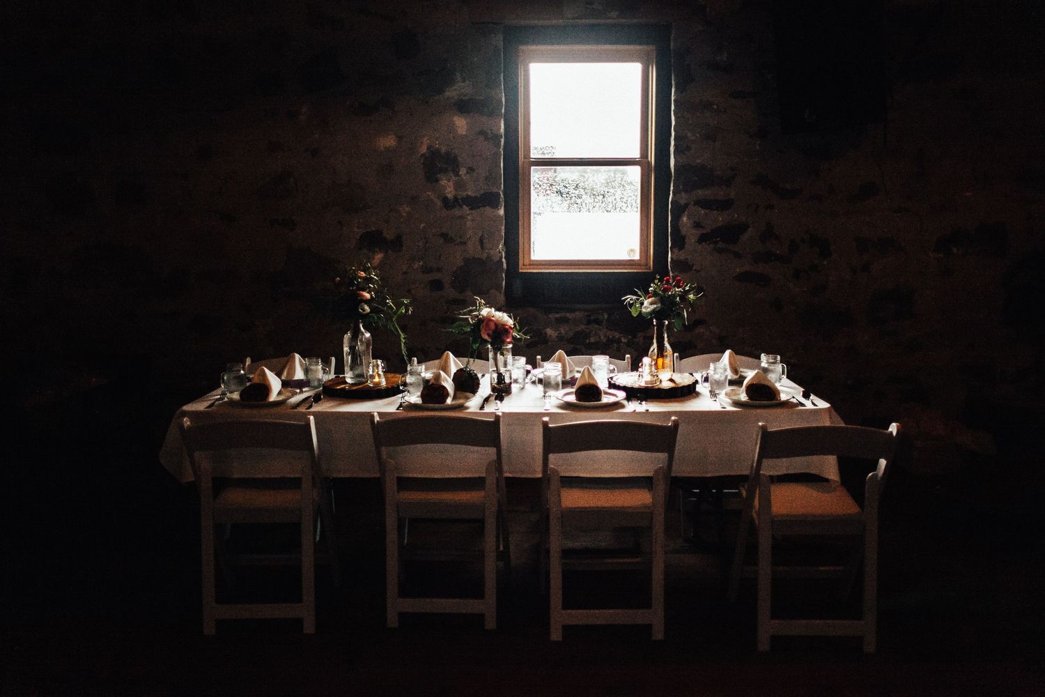 A rustic wooden dining table set in a dark room with elegant place settings and ambient lighting.