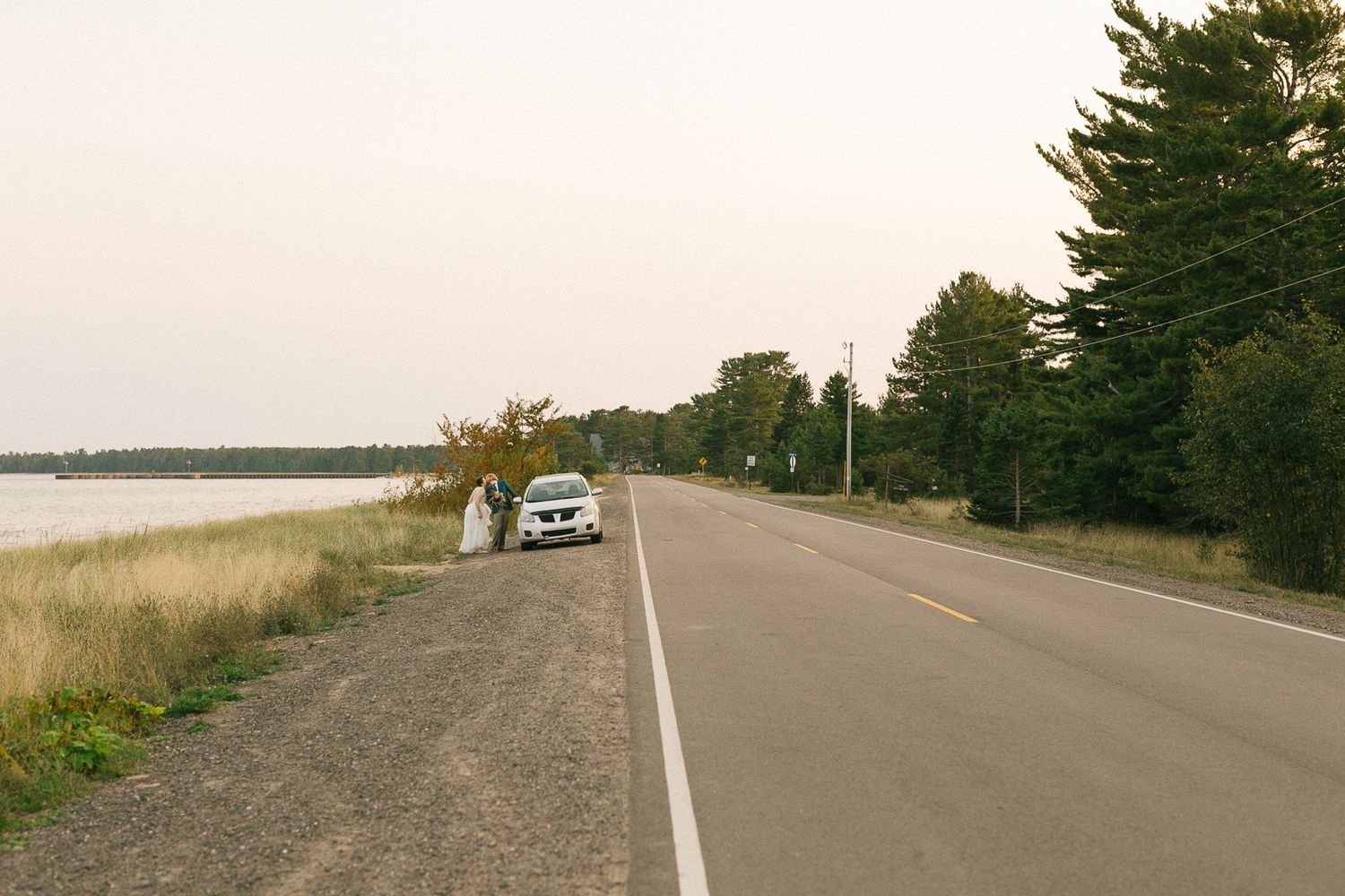 A long empty coastal road stretches into the distance with water views.