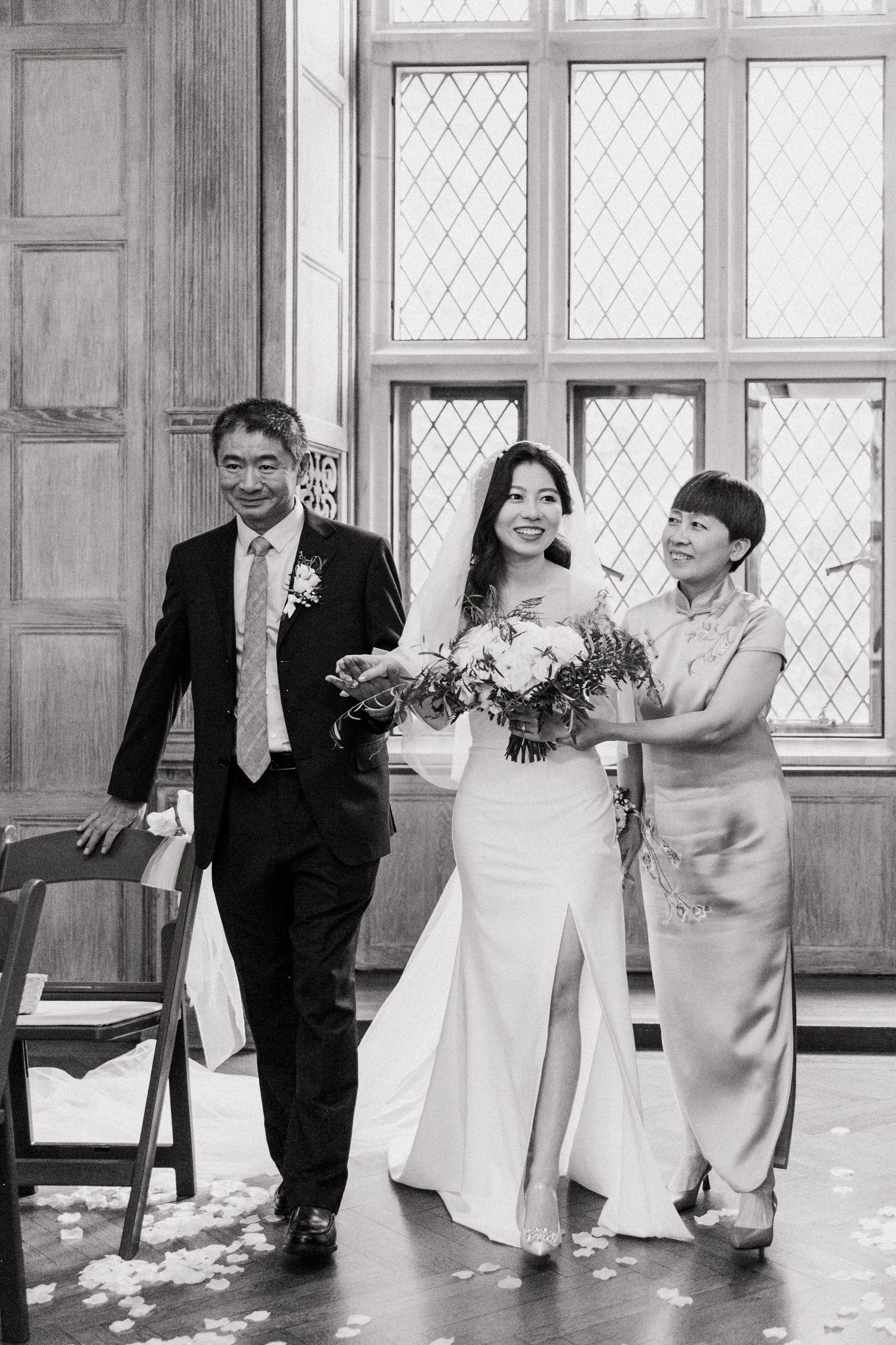 Bride walking down the aisle with parents in a black and white wedding photo.