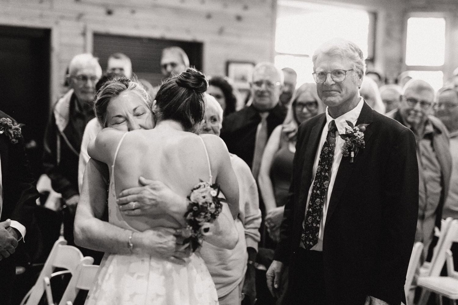 An intimate black and white wedding moment captured during a ceremony with guests looking on.