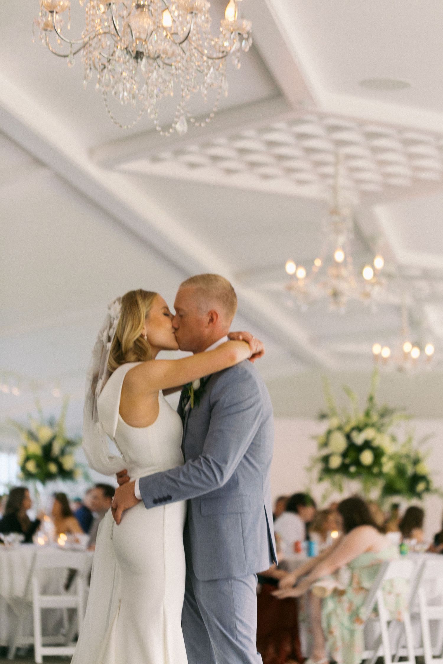 Romantic wedding reception moment under crystal chandeliers in bright white ballroom.