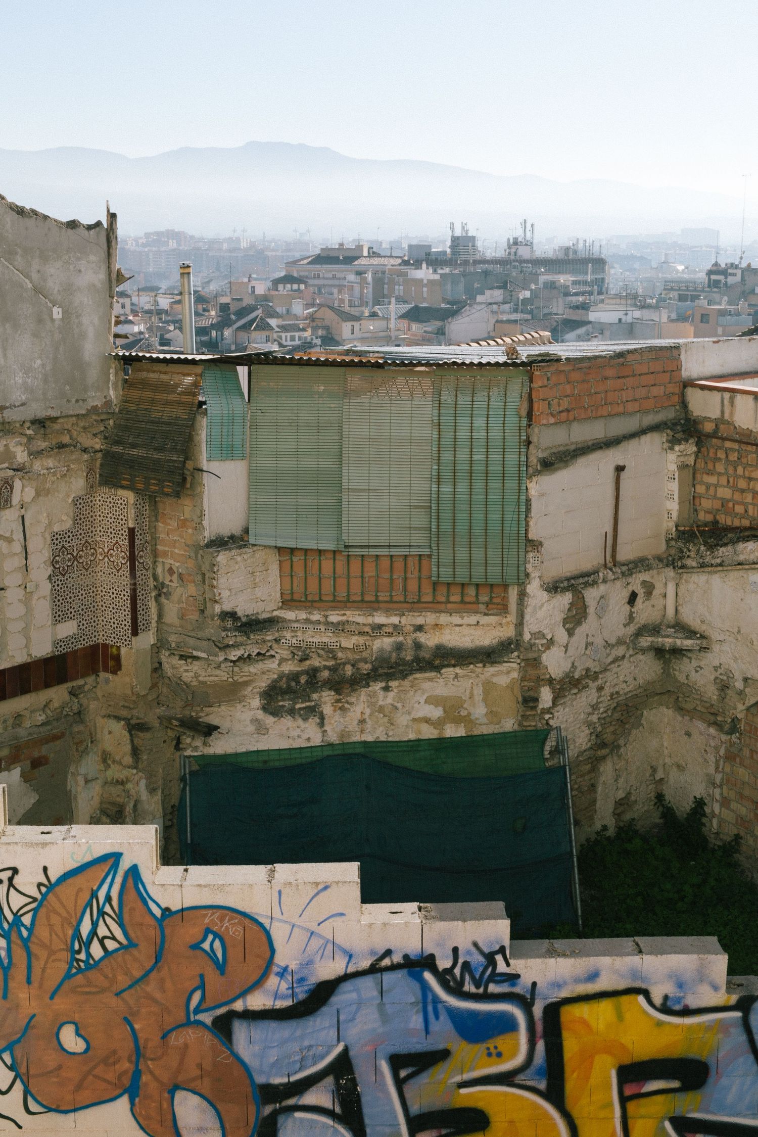 Urban cityscape showing graffiti art and dilapidated buildings with mountains visible in the hazy distance.