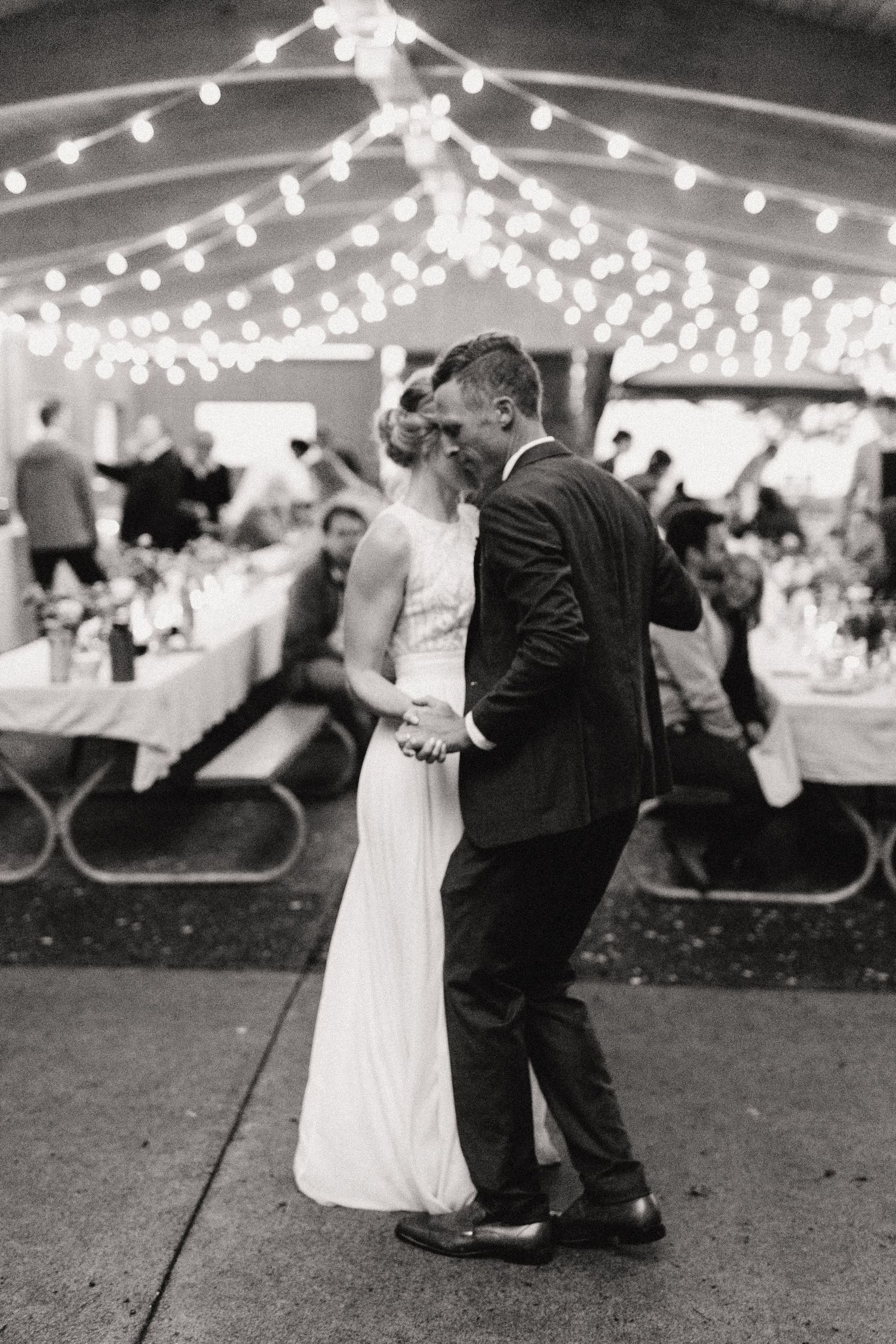 Wedding couple sharing their first dance under twinkling lights at outdoor reception.