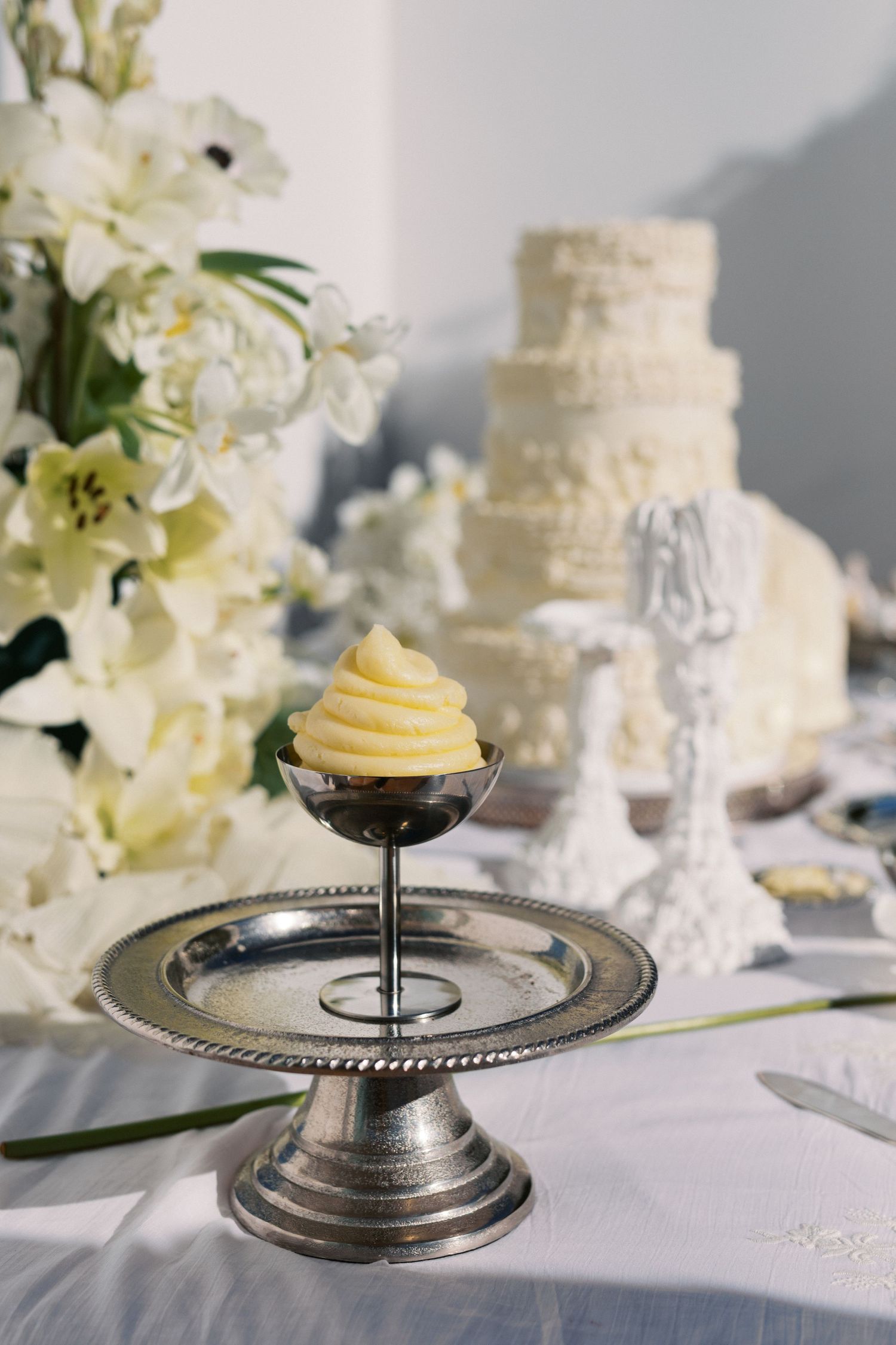 Elegant wedding dessert table with a cupcake on silver stand, white tiered cake, and floral arrangements.