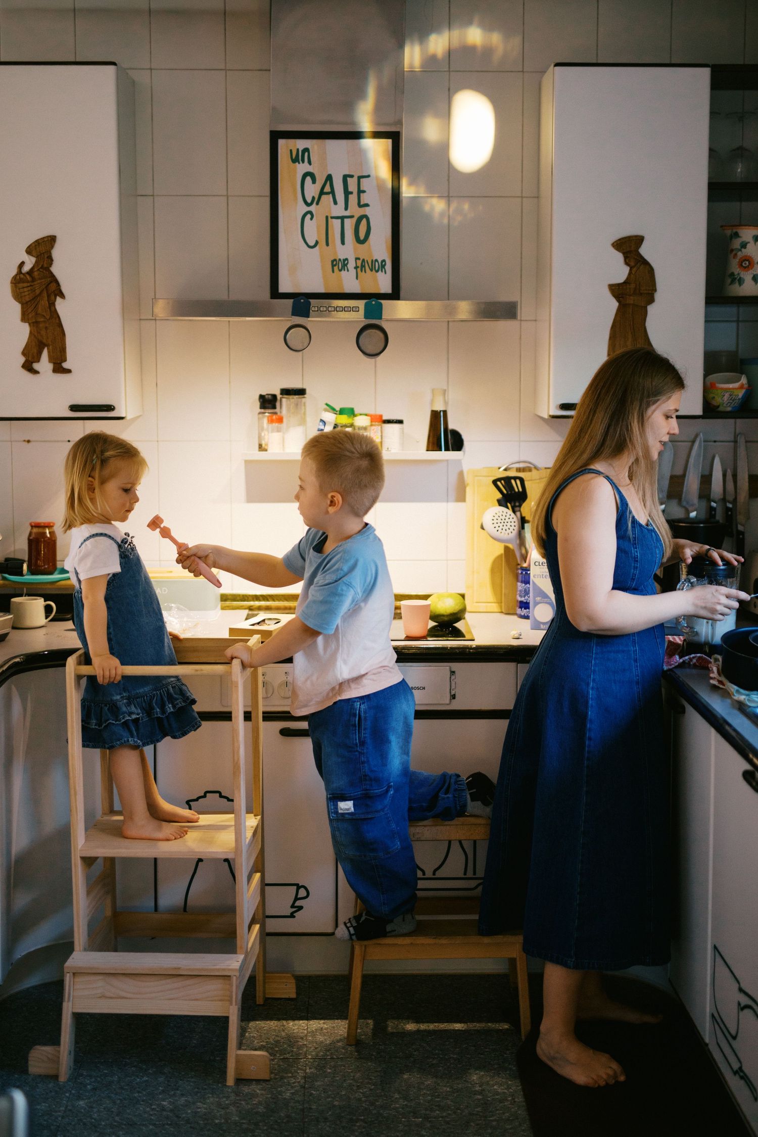 Mother and two young children cooking together in modern white kitchen on learning towers.