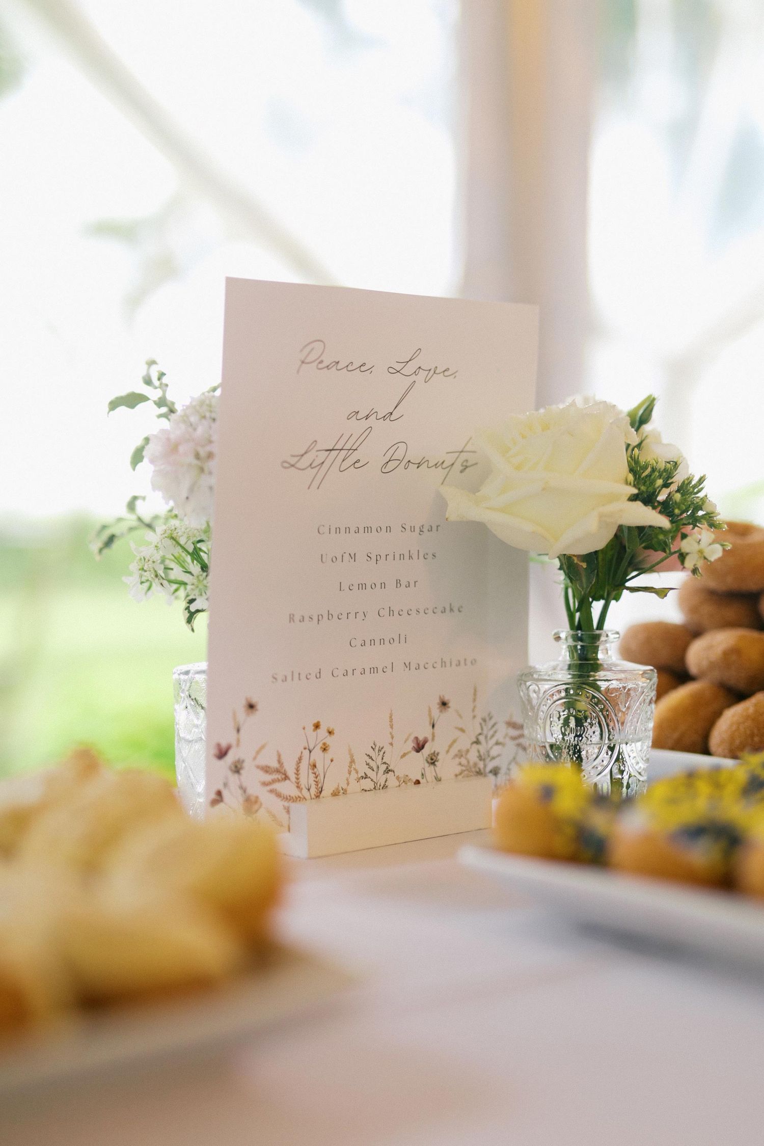 Elegant wedding place cards with calligraphy text displayed on a white table with floral decorations and pastries in soft focus.