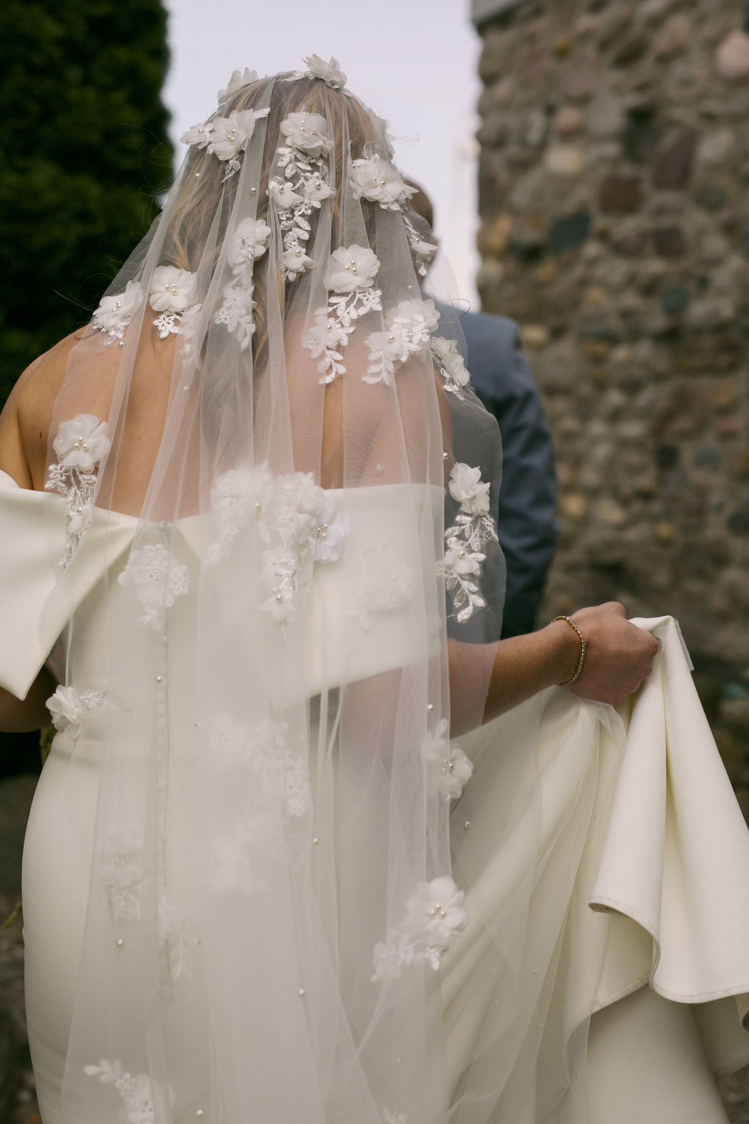 Delicate lace veil with floral appliques flowing against a white wedding dress.