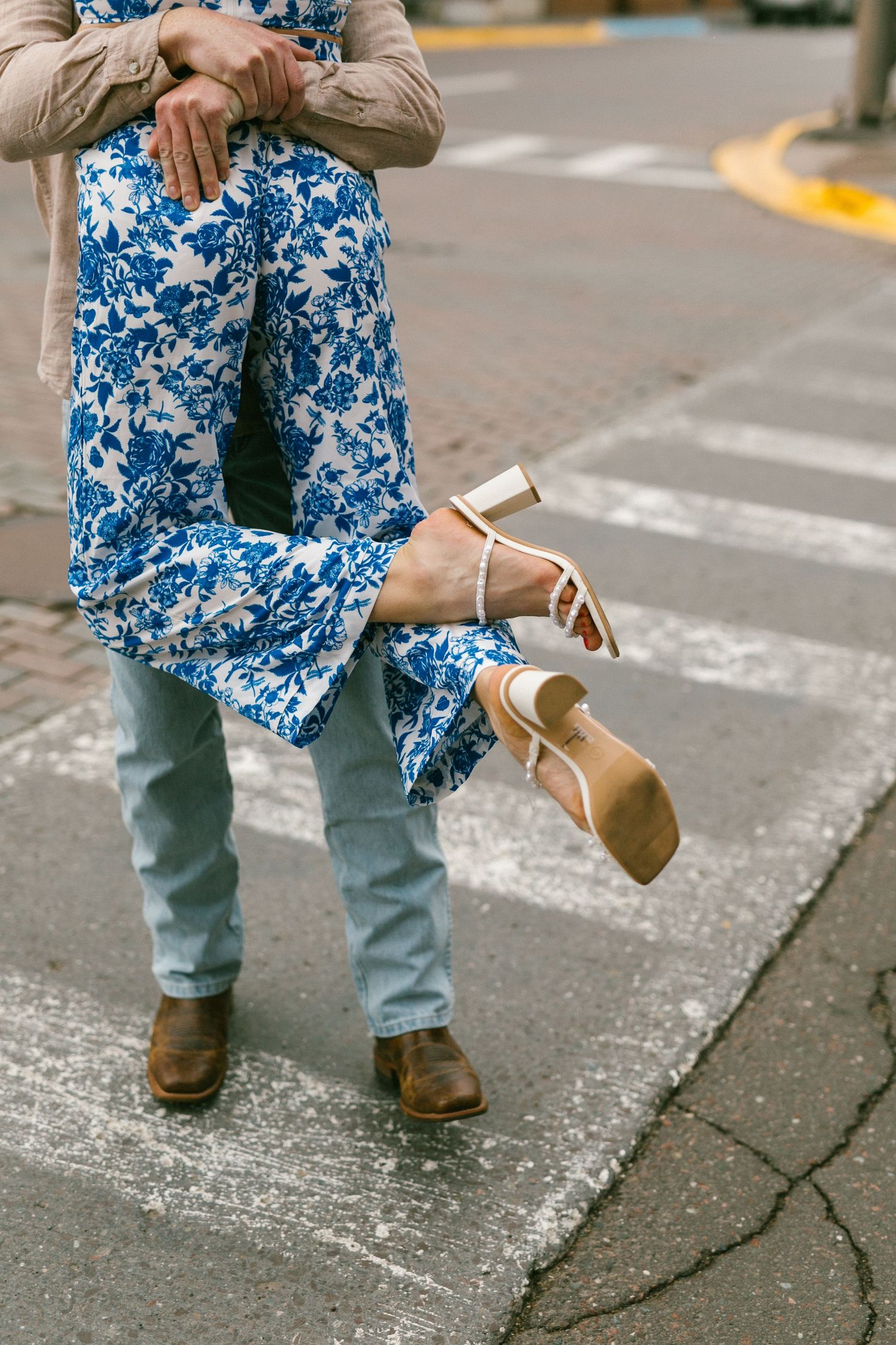 Person wearing blue floral pants and tan shoes stands on a sidewalk curb while being lifted.