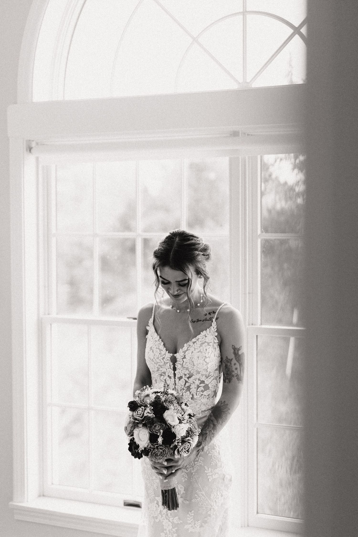 A romantic black and white bridal portrait near a sunlit window with a beautiful floral bouquet.