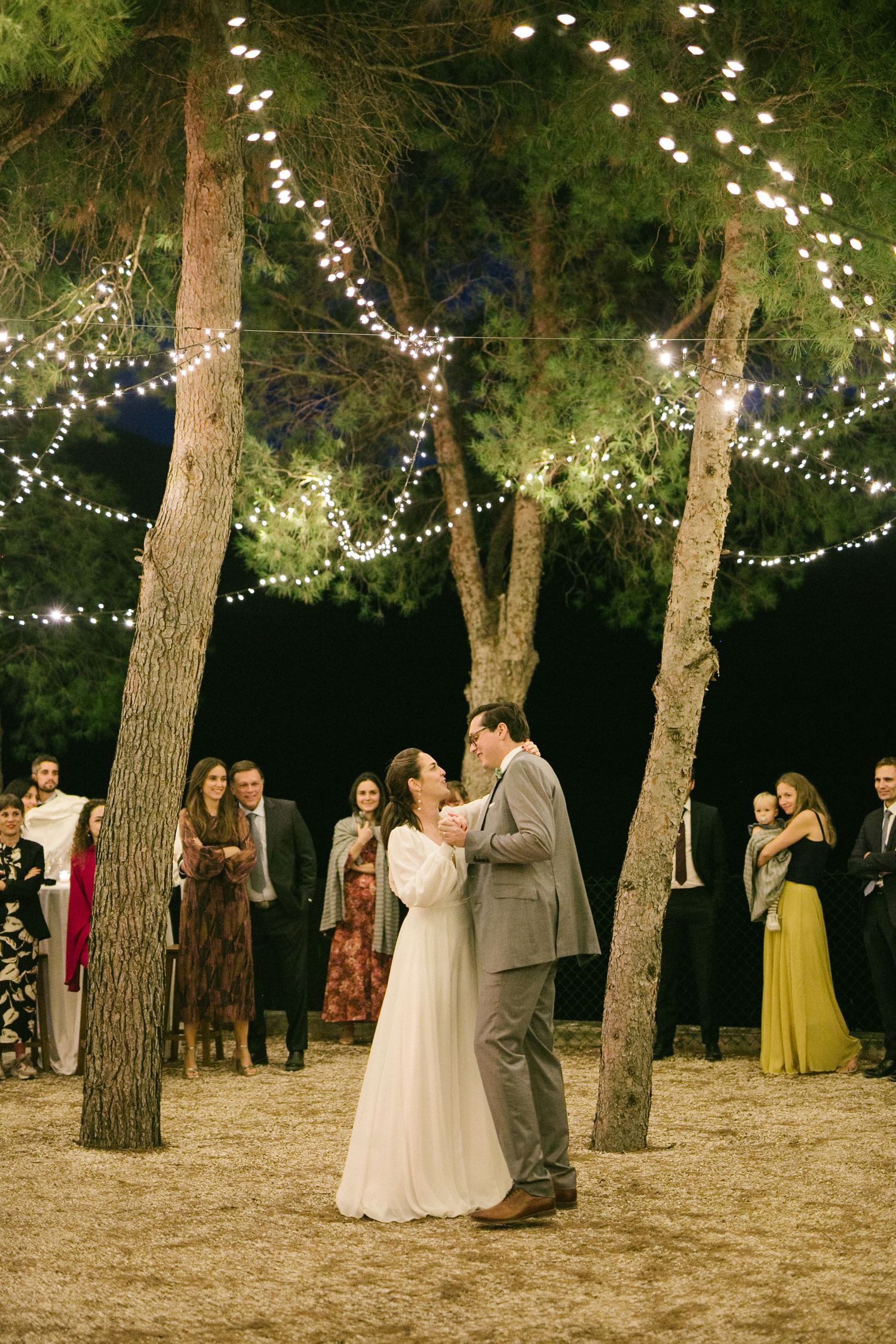 A romantic outdoor evening wedding ceremony under string lights wrapped between tall trees. Europe and Spain destination wedding photography