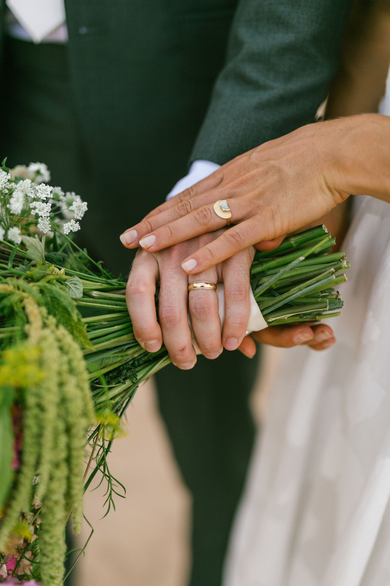 Wedding rings and hands holding a fresh bouquet of white flowers with greenery.