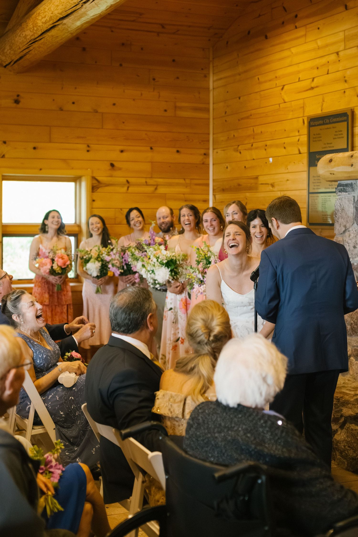 Wedding guests share joyful laughter during a reception in a rustic wooden cabin venue.