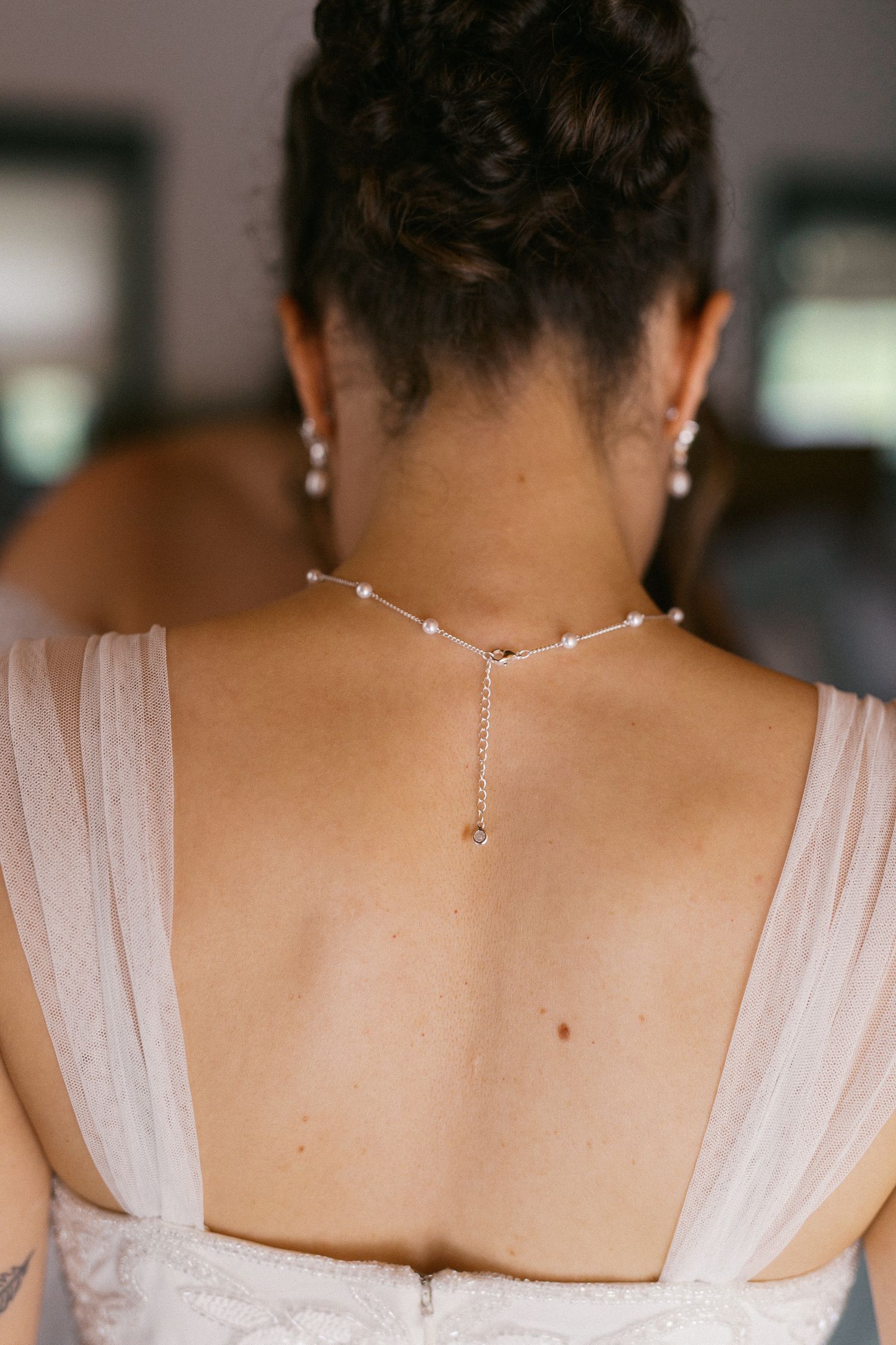 Bride wearing elegant back necklace with pearls and chain detail, updo hairstyle, backless white wedding dress.