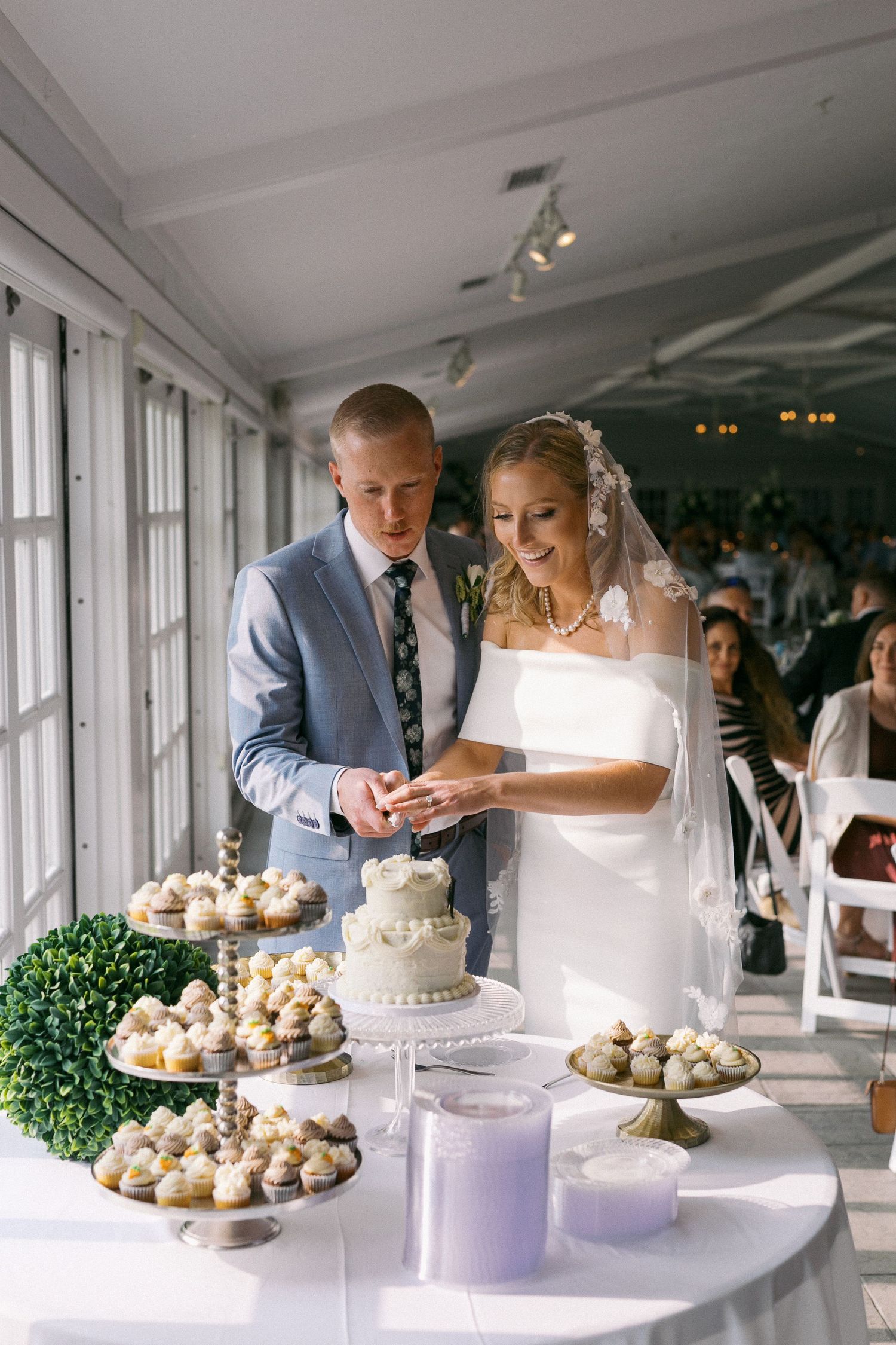 Beautiful dessert table at a wedding reception features elegant white cupcakes and decorative greenery on a white tablecloth.