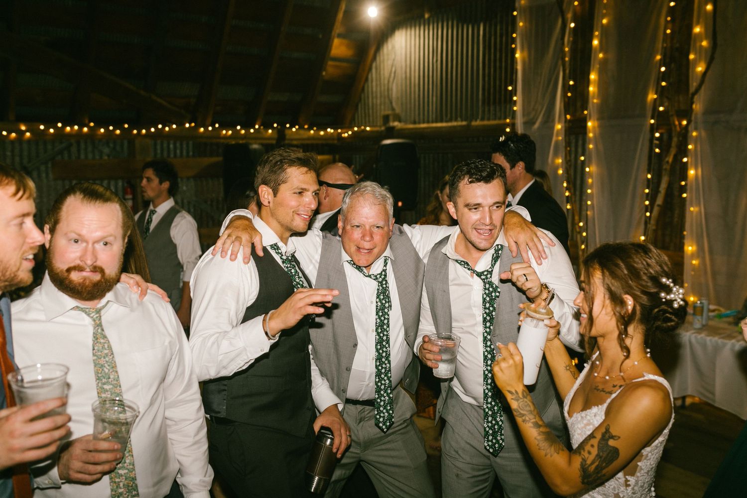 Wedding guests celebrate and dance together at an evening reception decorated with string lights and festive decor.